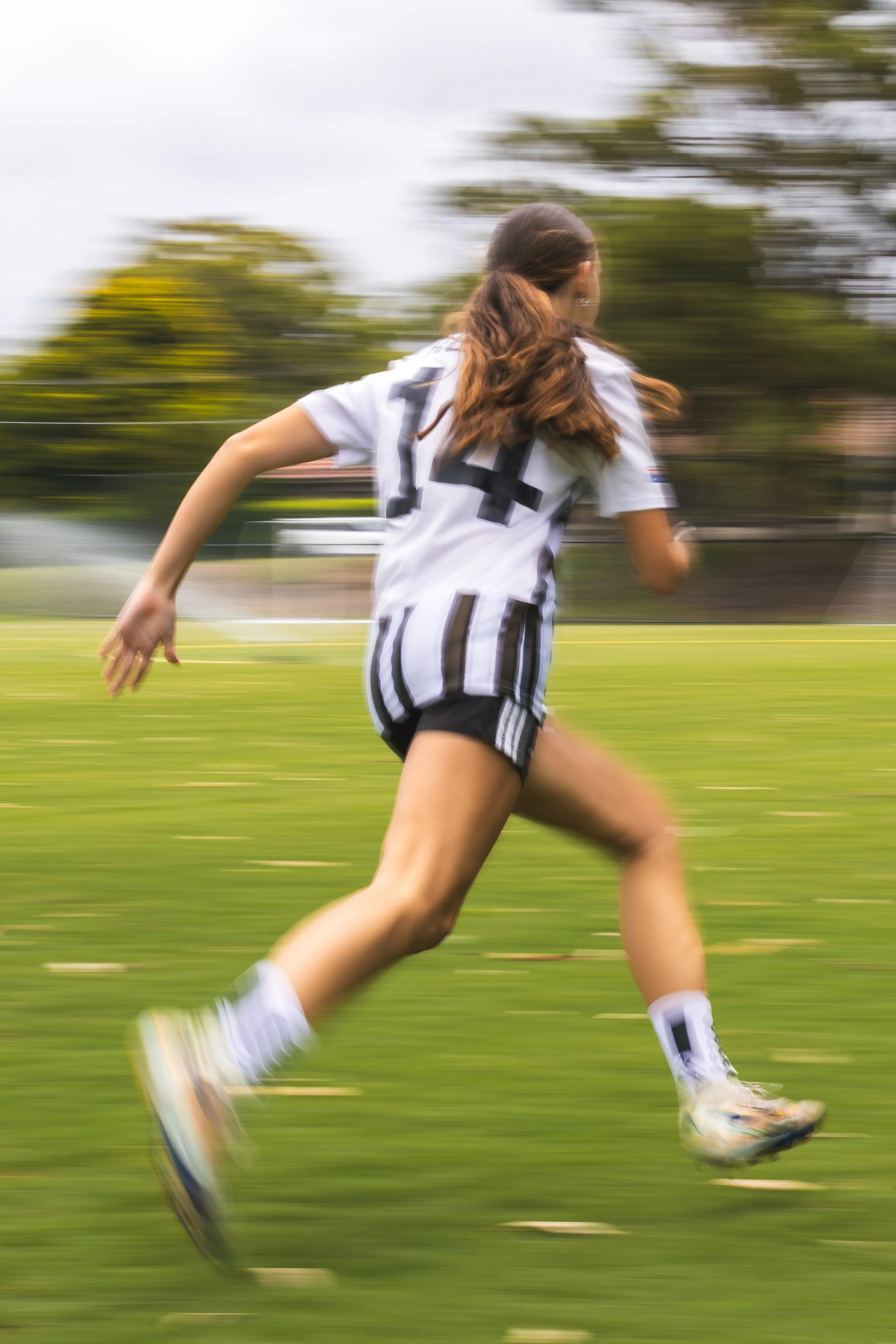 A person in a sports uniform running on a grassy field, with motion blur indicating speed.