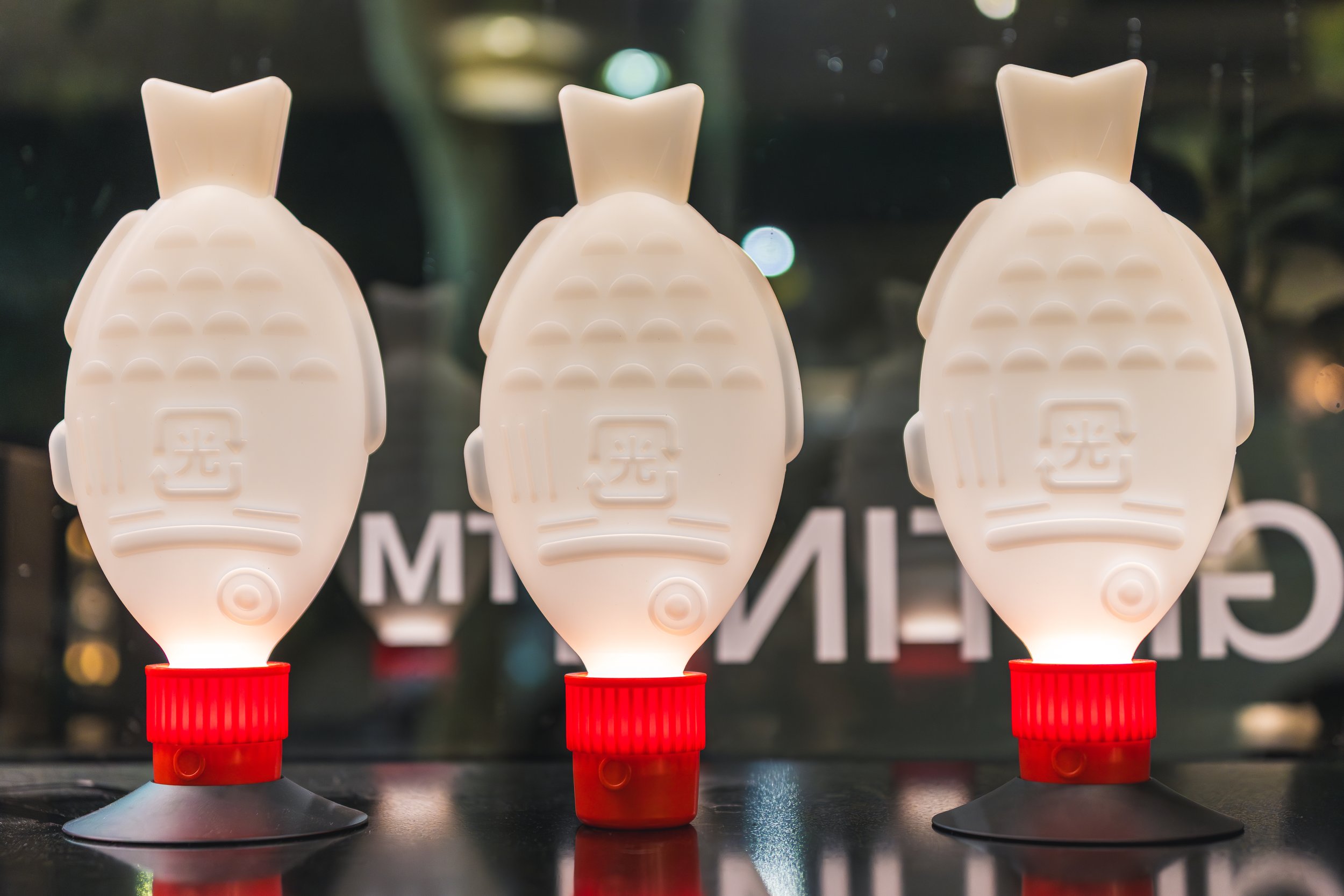 Three white pineapple-shaped objects on red and black stands with a background of blurred lights and text.