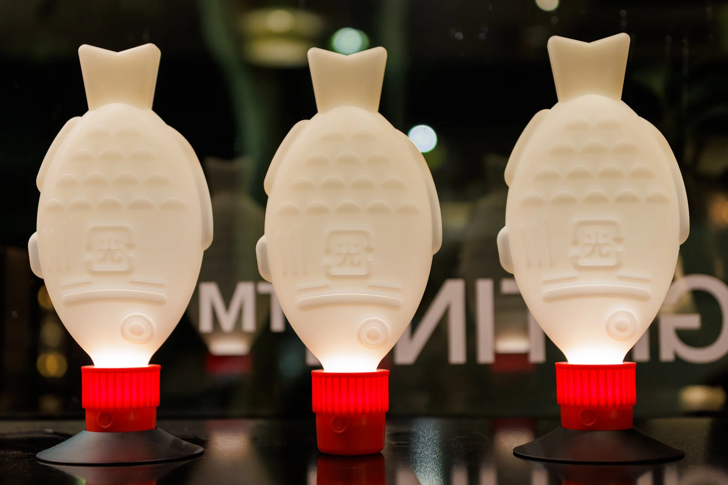 Three upbeat Totoro-shaped nightlights with red bases illuminated in a dark room.