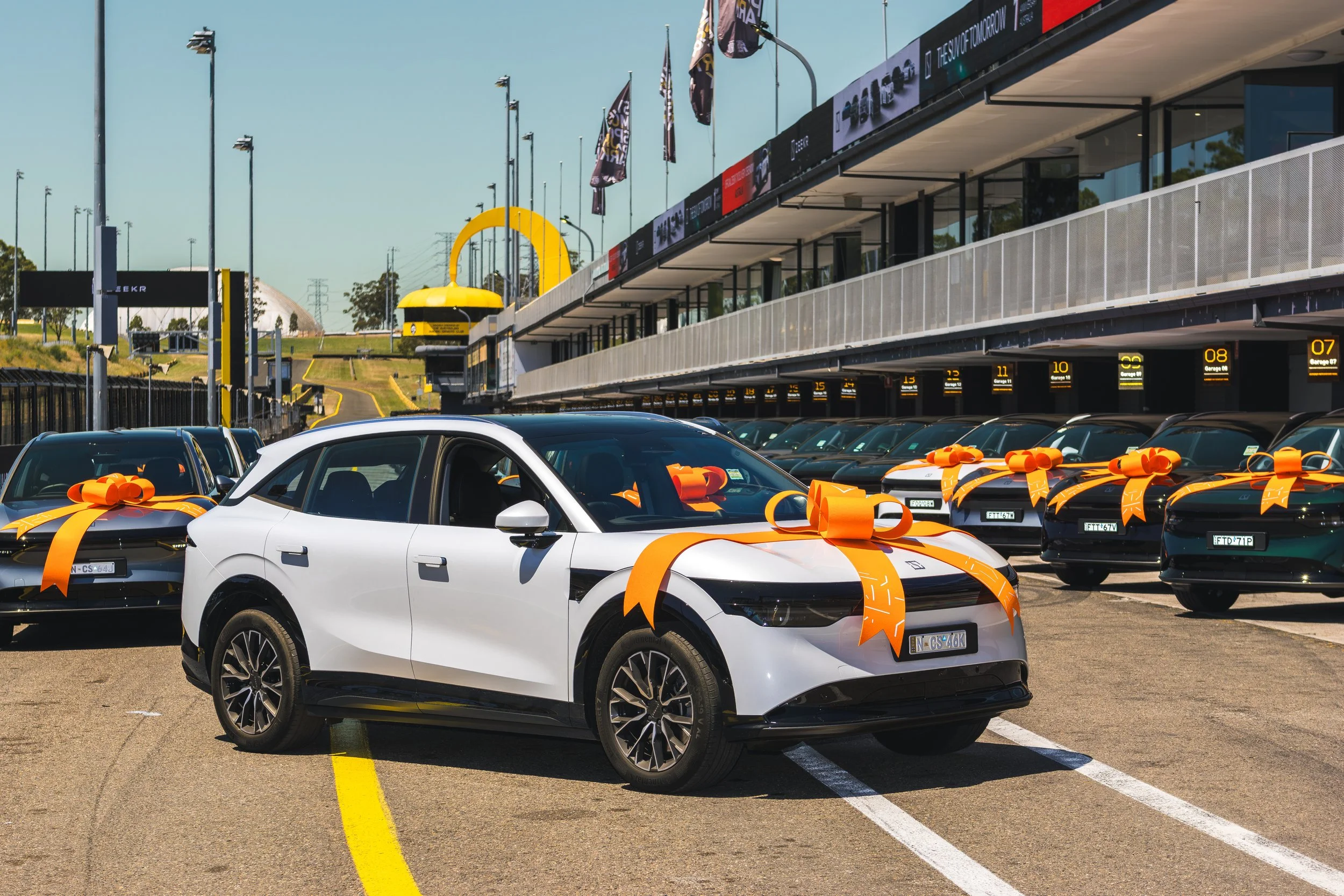 Multiple cars in a parking lot decorated with orange ribbons and bows.