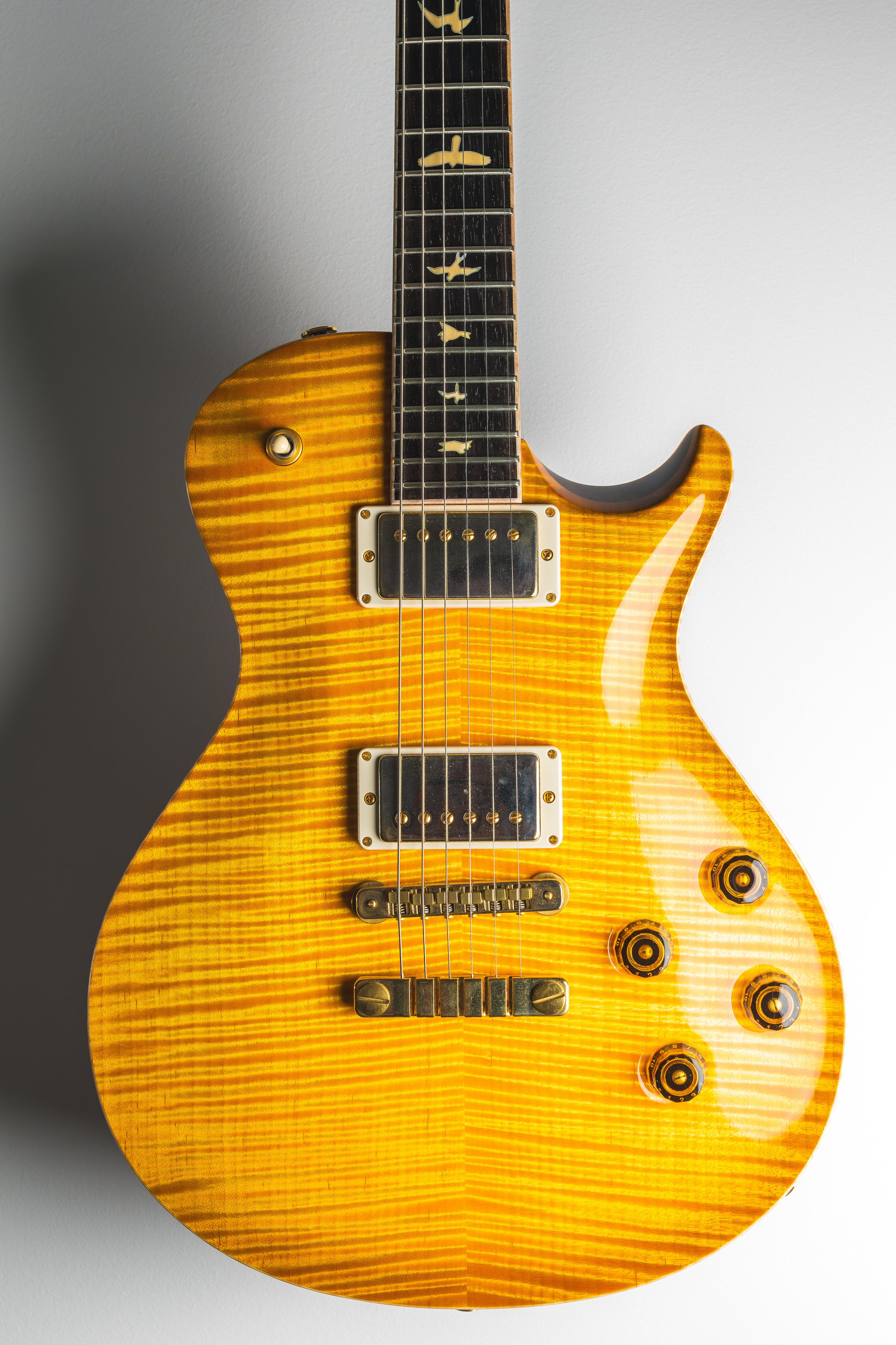 A yellow electric guitar with a striped wood grain pattern, six control knobs, two pickups, and a bridge, against a plain, light gray background.