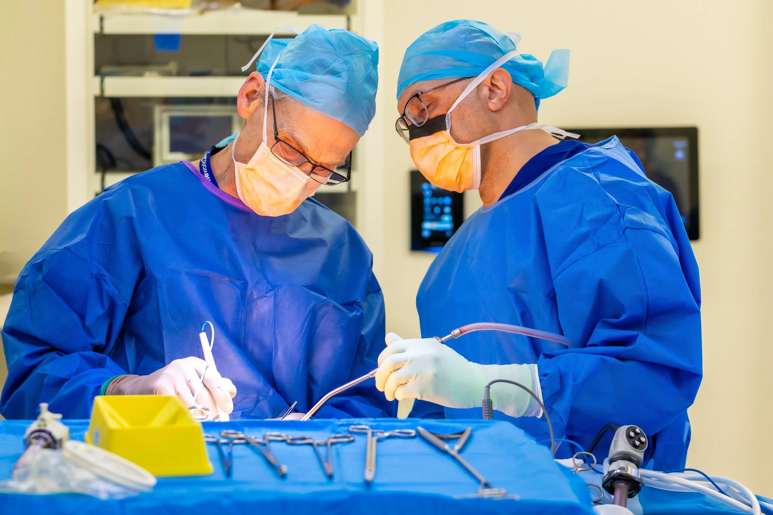 Two surgeons in blue scrubs, surgical masks, and caps performing an operation in an operating room.