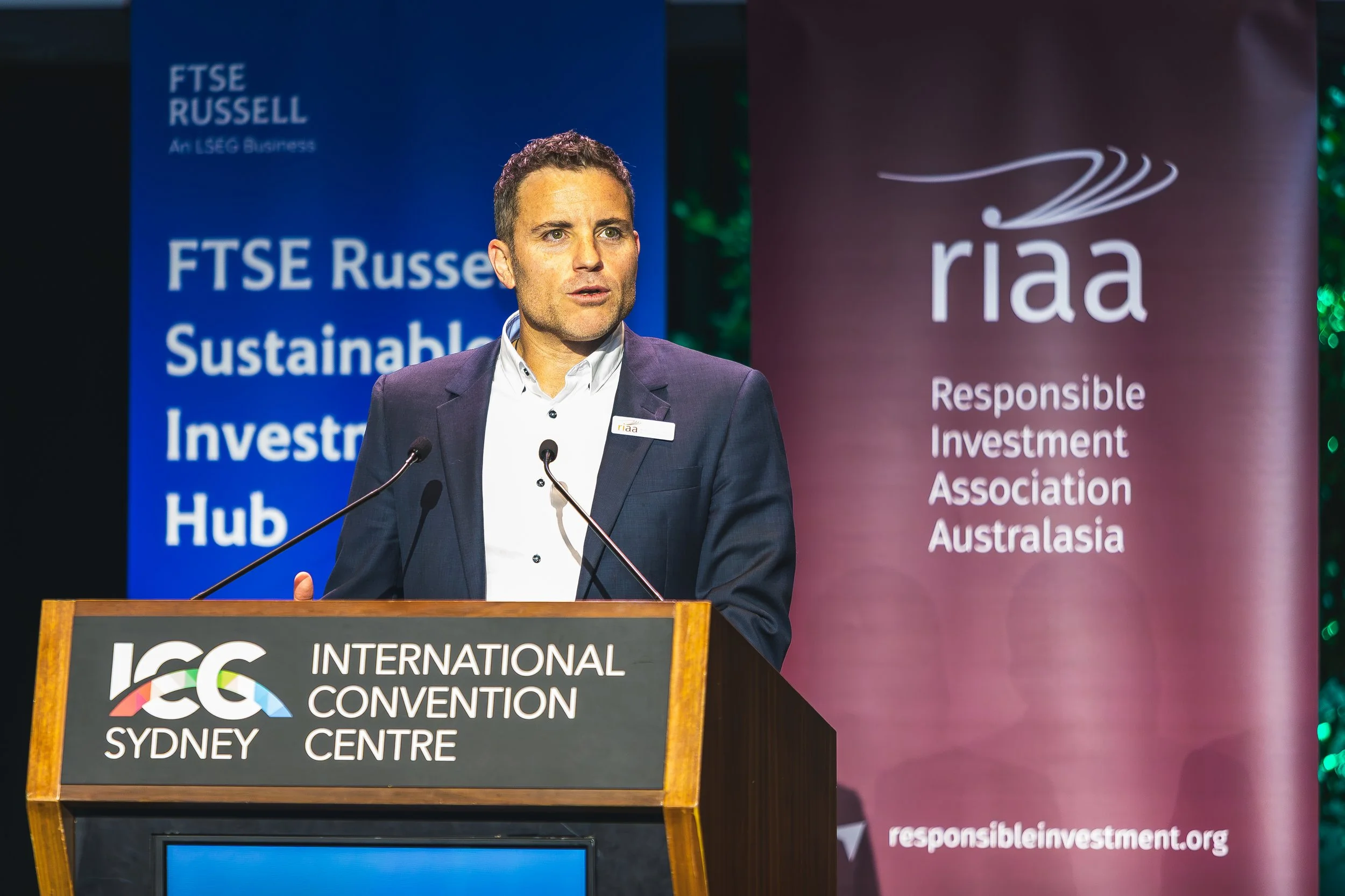 A man in a suit speaking at a podium during the International Convention at ICC Sydney. Behind him are banners for FTSE Russell and Responsible Investment Australia.