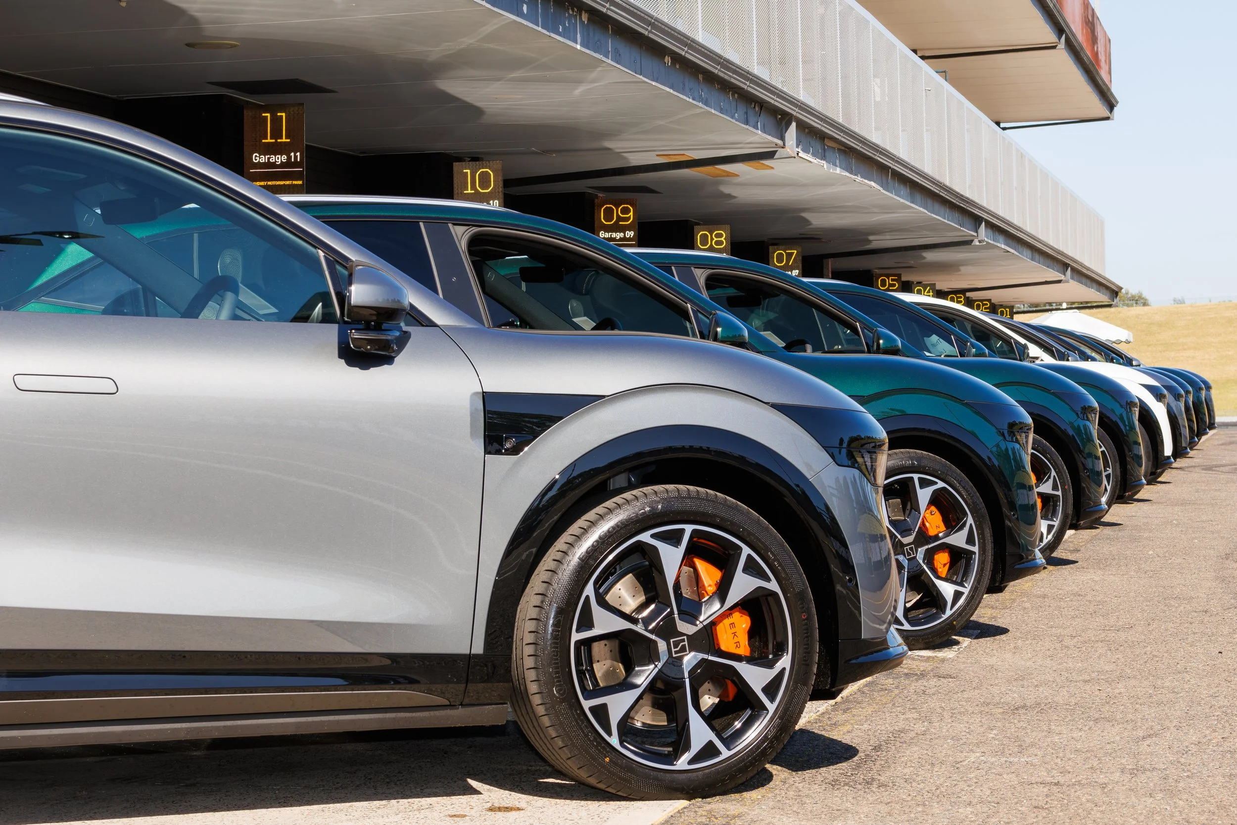 Multiple cars parked in a row underneath a parking garage with yellow labeled digital signs showing garage levels from 01 to 11.