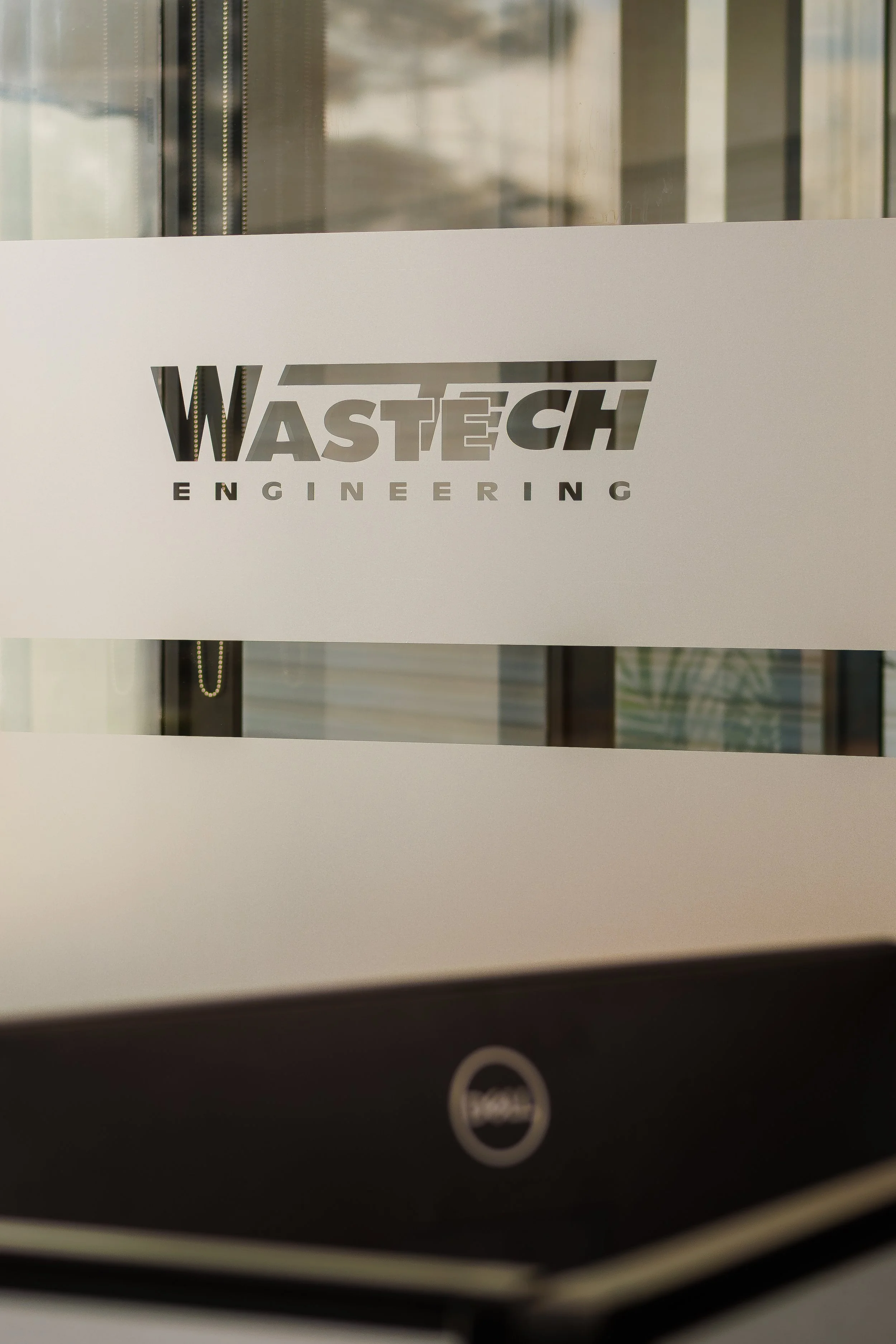 Close-up of a white sign with the 'WASTECH ENGINEERING' logo, partially covering a glass door or window.