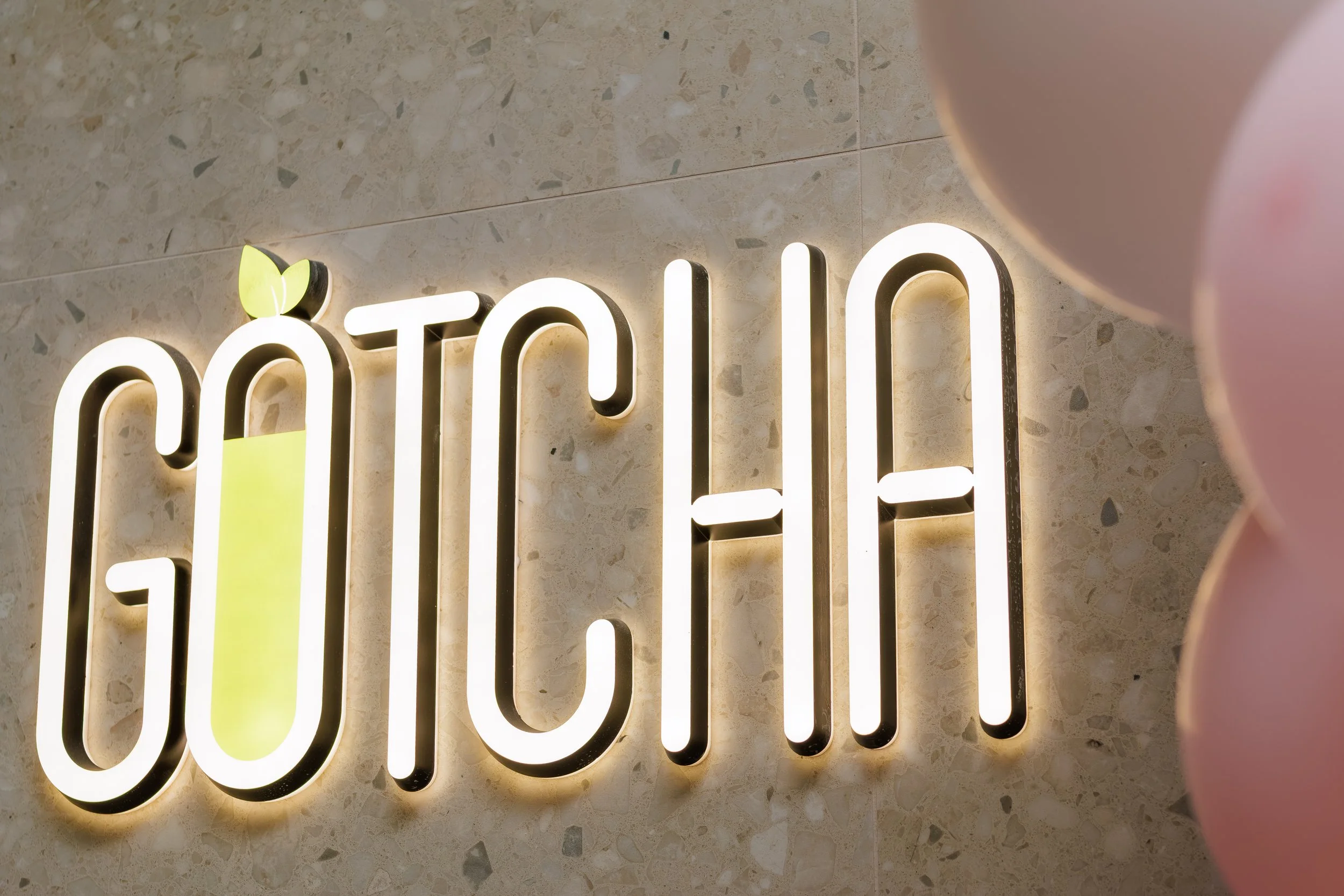 Illuminated sign displaying the word 'good' on a marble wall, with part of a pink object in the foreground.