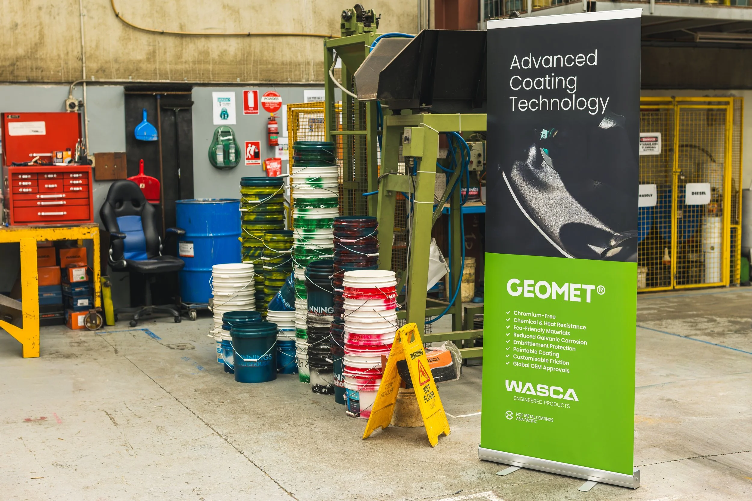 Industrial warehouse with buckets of paint, safety equipment, and a large sign promoting advanced coating technology and engineered products.