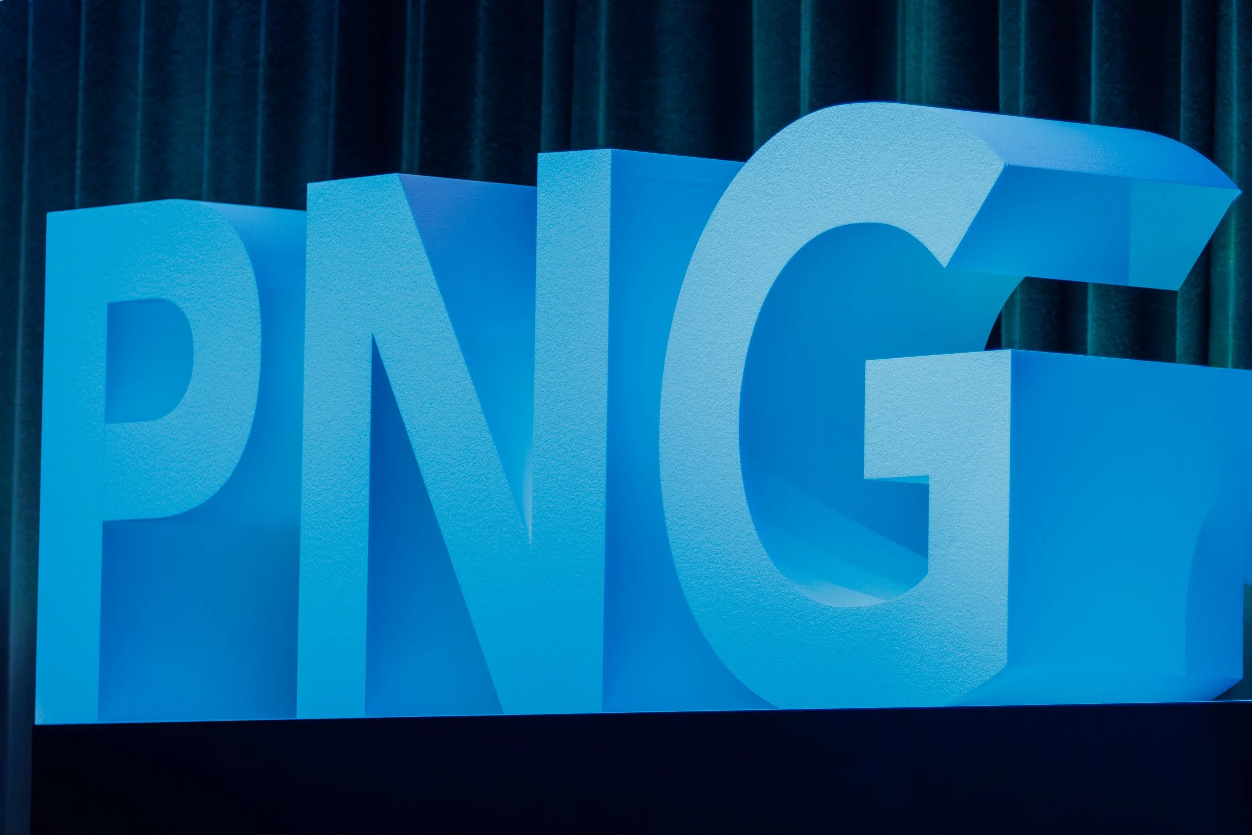 Close-up of blue 3D letters spelling 'NYC' against a dark green curtain background.