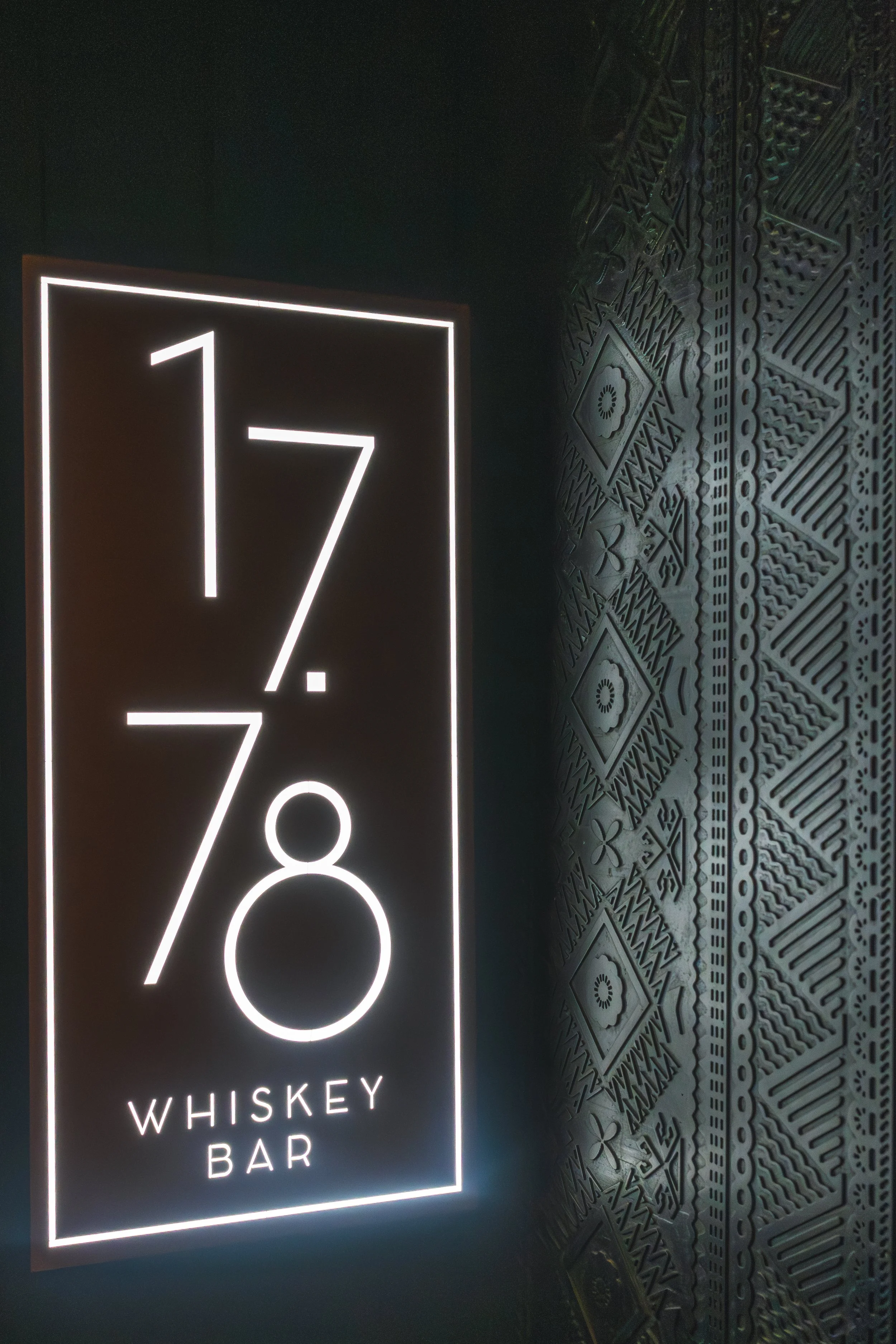 Neon sign displays the word 'Whiskey' and 'Bar' with part of a diamond pattern wall in the background.