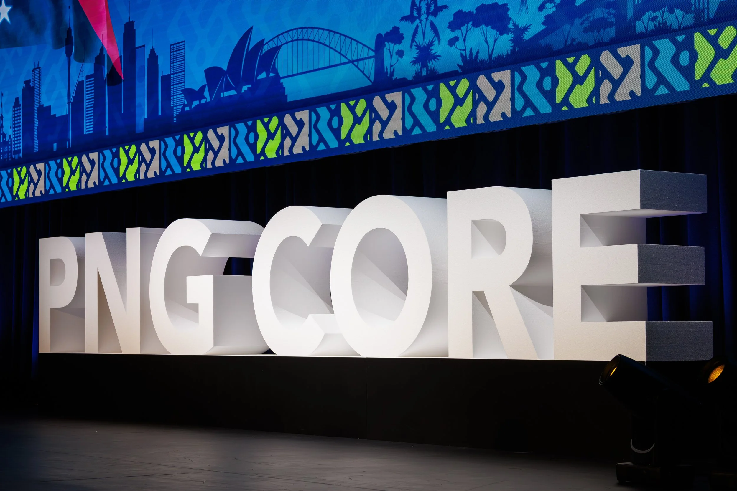 Large 3D white letters spelling 'NECTAR' in front of a backdrop featuring city buildings, a bridge, and trees with a colorful top border showing urban and nature silhouettes at night.