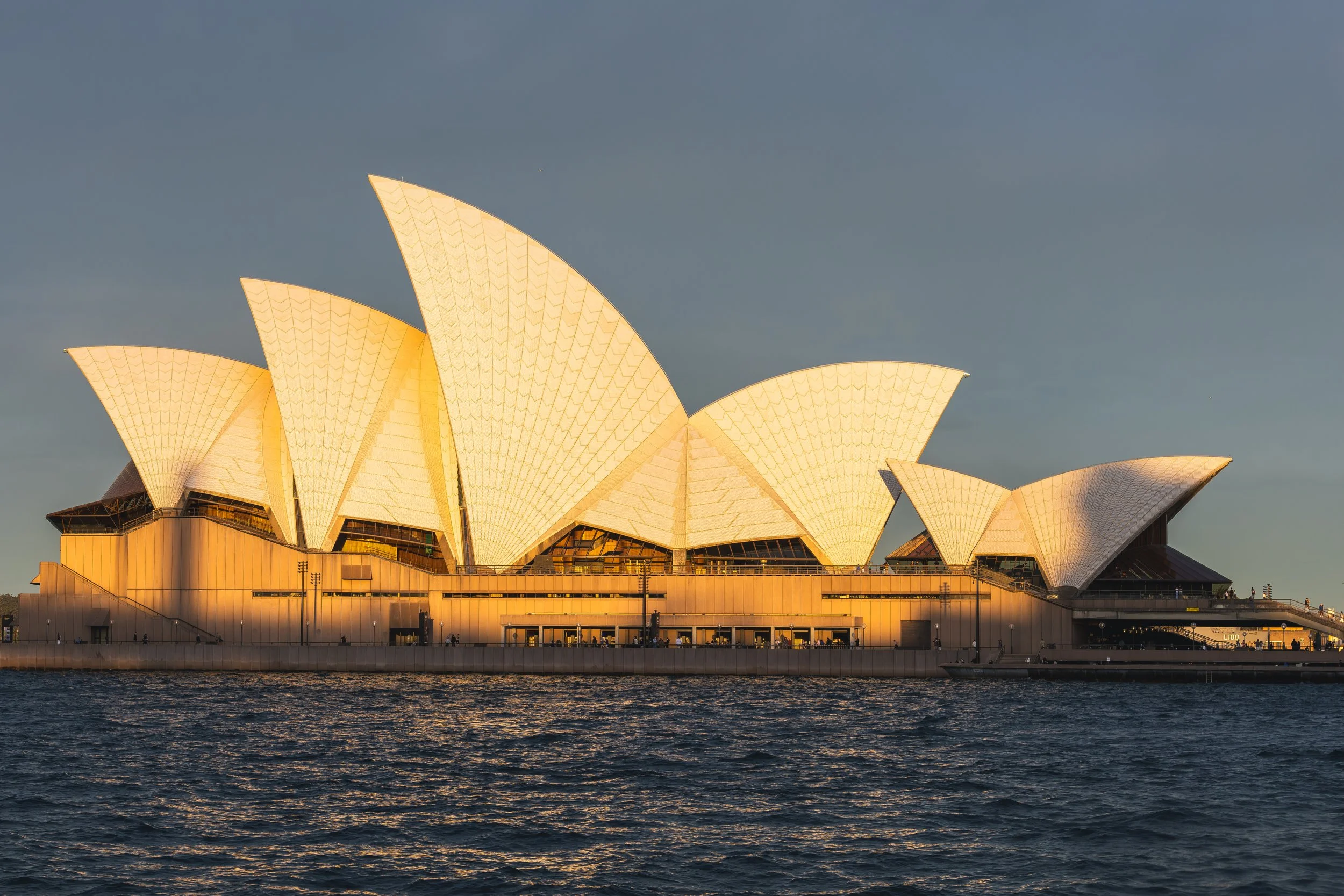 Sydney Opera House illuminated at sunset with reflections on the water in the foreground.