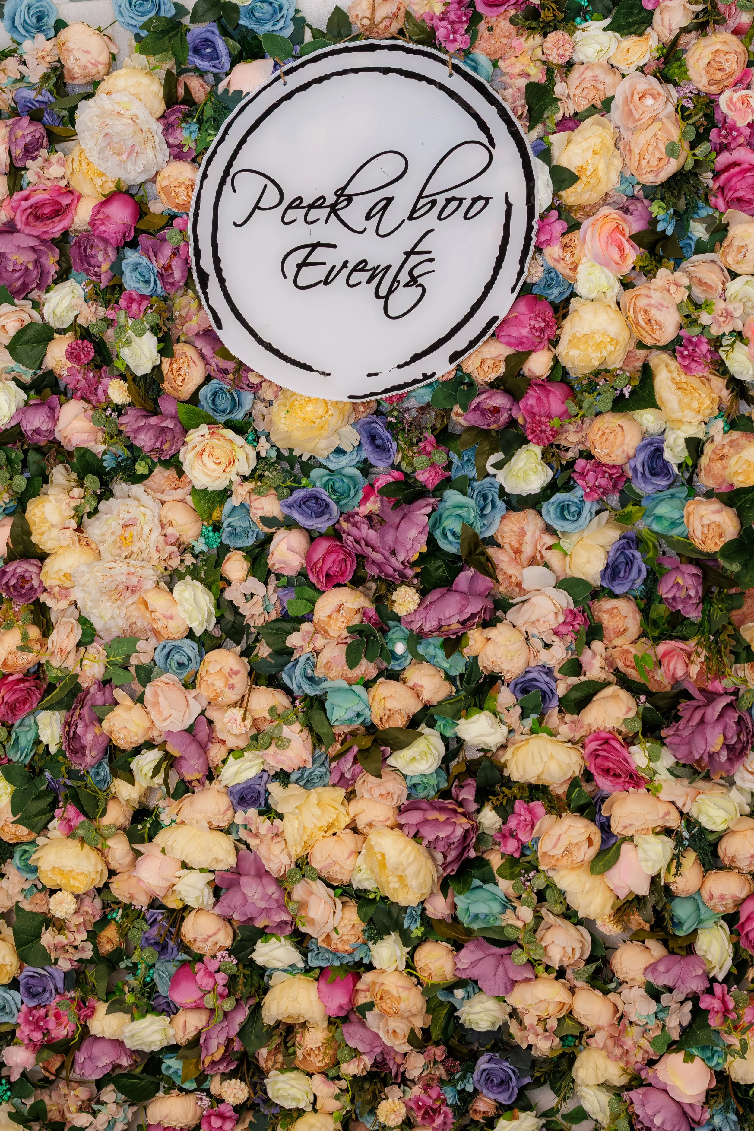 A floral backdrop with a circular sign that reads 'Peekaboo Events' in elegant black cursive font.
