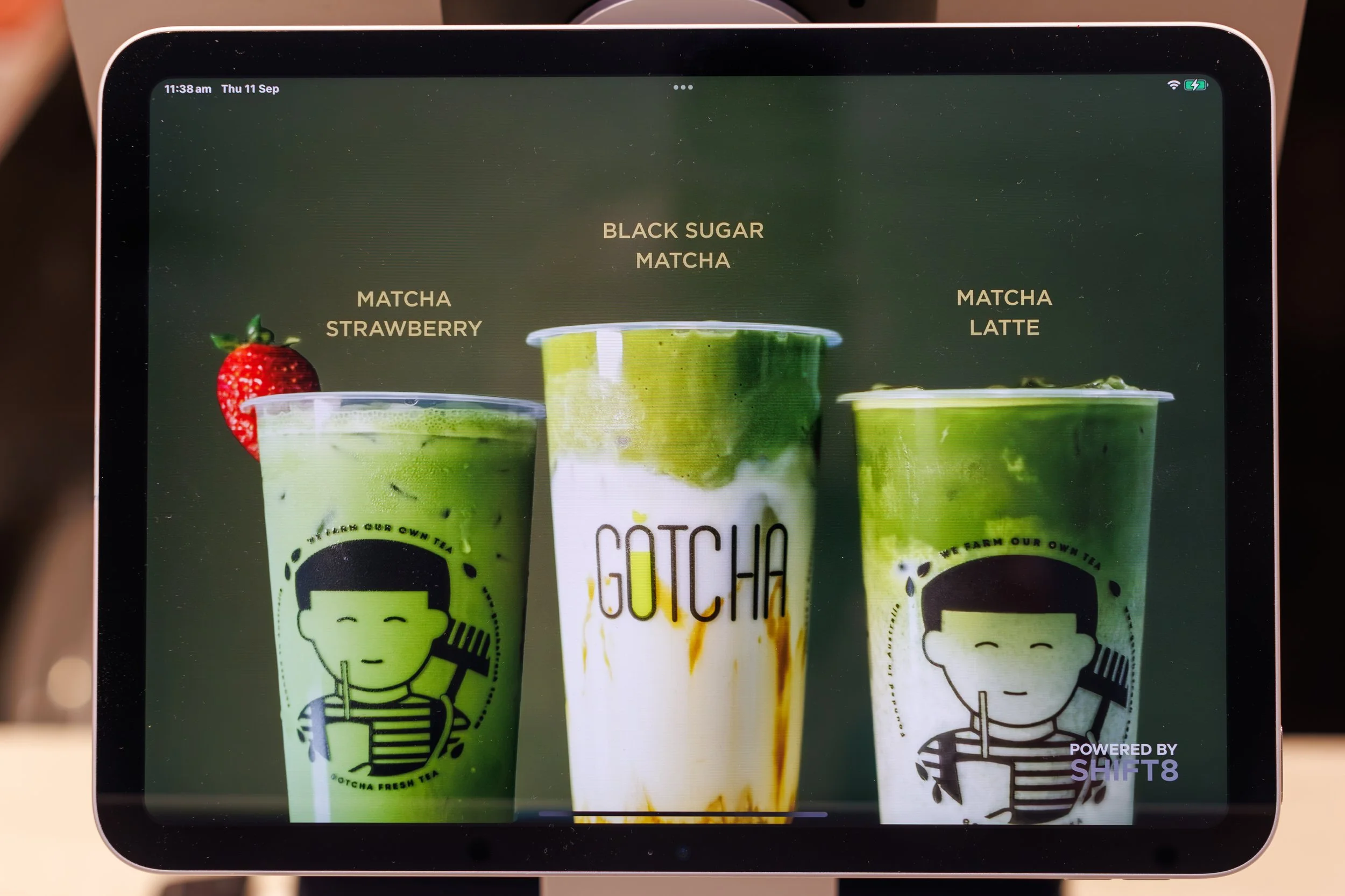 Display screen showing three green matcha beverages with various flavors listed above: Strawberry, Black Sugar Matcha, and Matcha Latte, with a strawberry garnishing the left drink.
