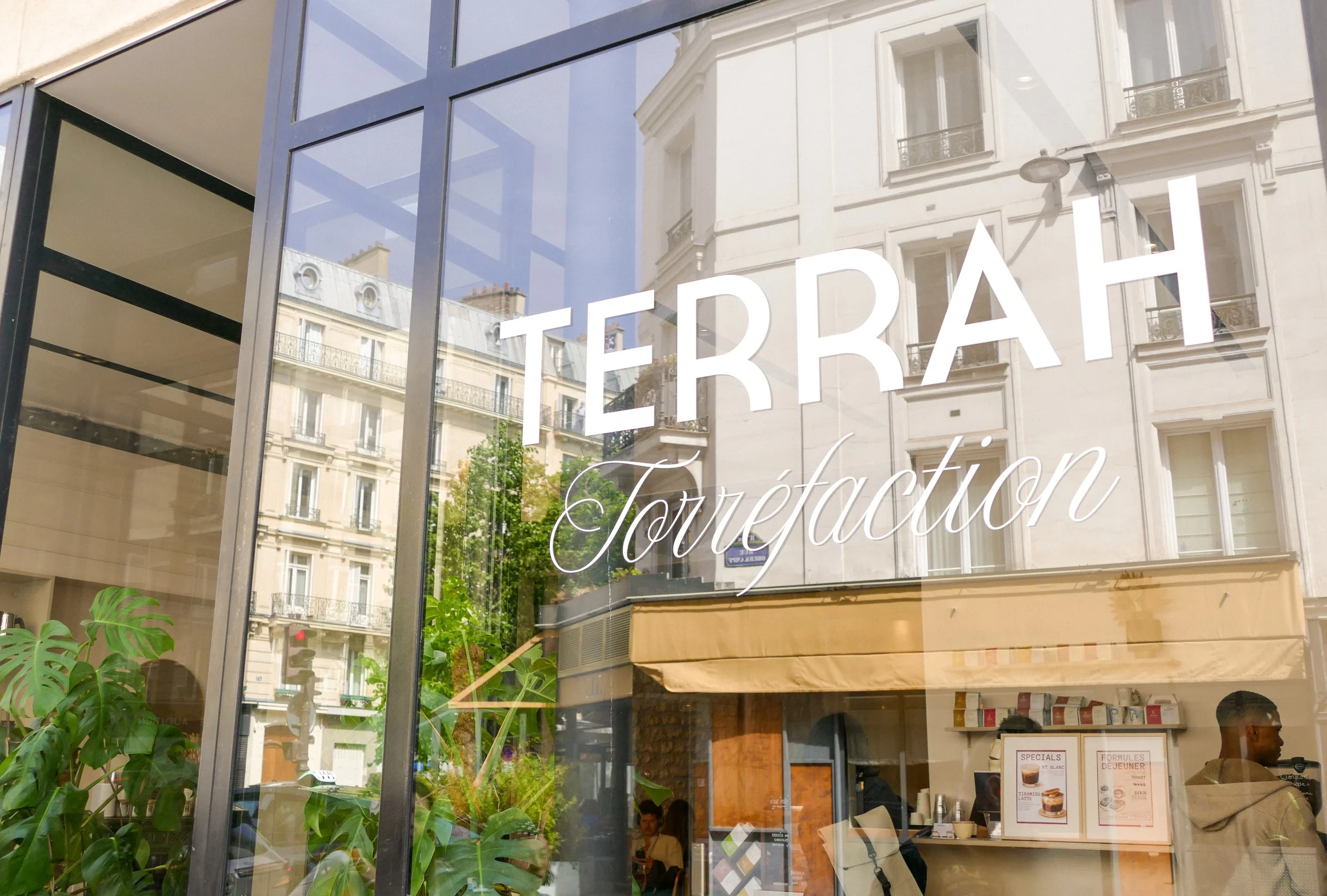 Storefront window with the name 'TERRAH' and the word 'Tortéction' underneath, reflecting surrounding buildings and a street scene.
