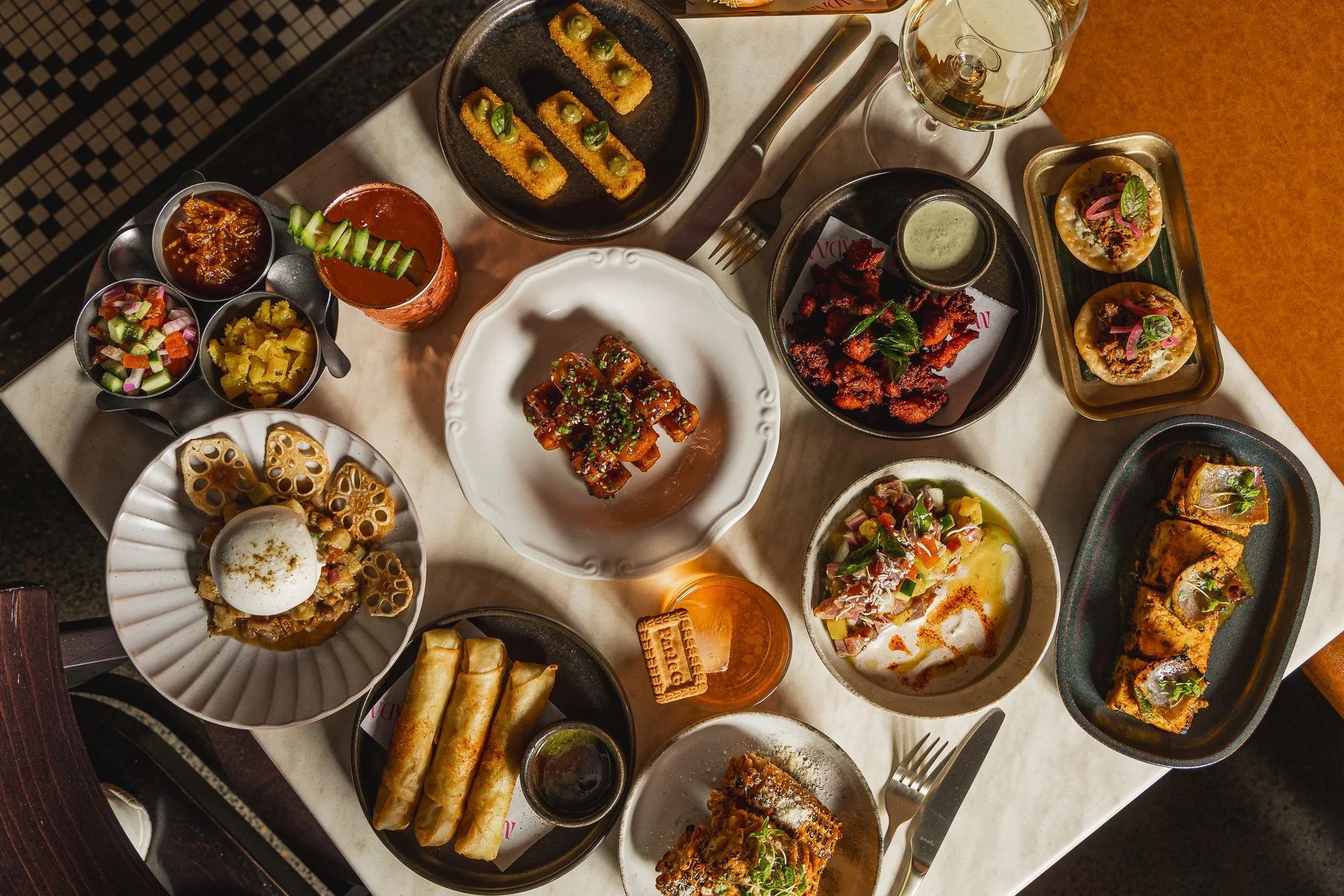 Top down shot of table full of modern Indian food and cocktails at Madam Ji
