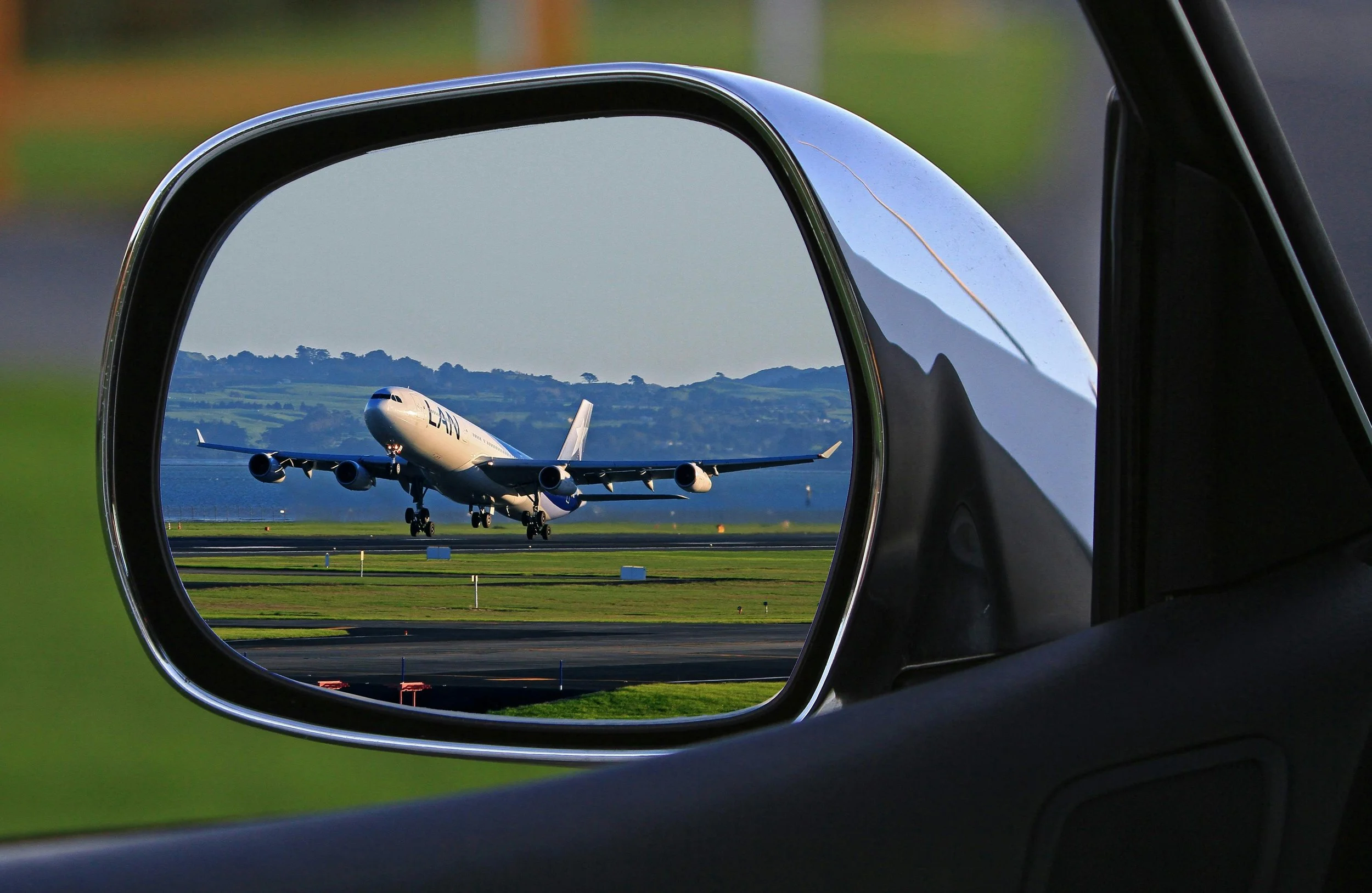 Taxi in Makry Gialos & Ierapetra - An airplane landing on a runway, captured through the side mirror of a vehicle at the airport.