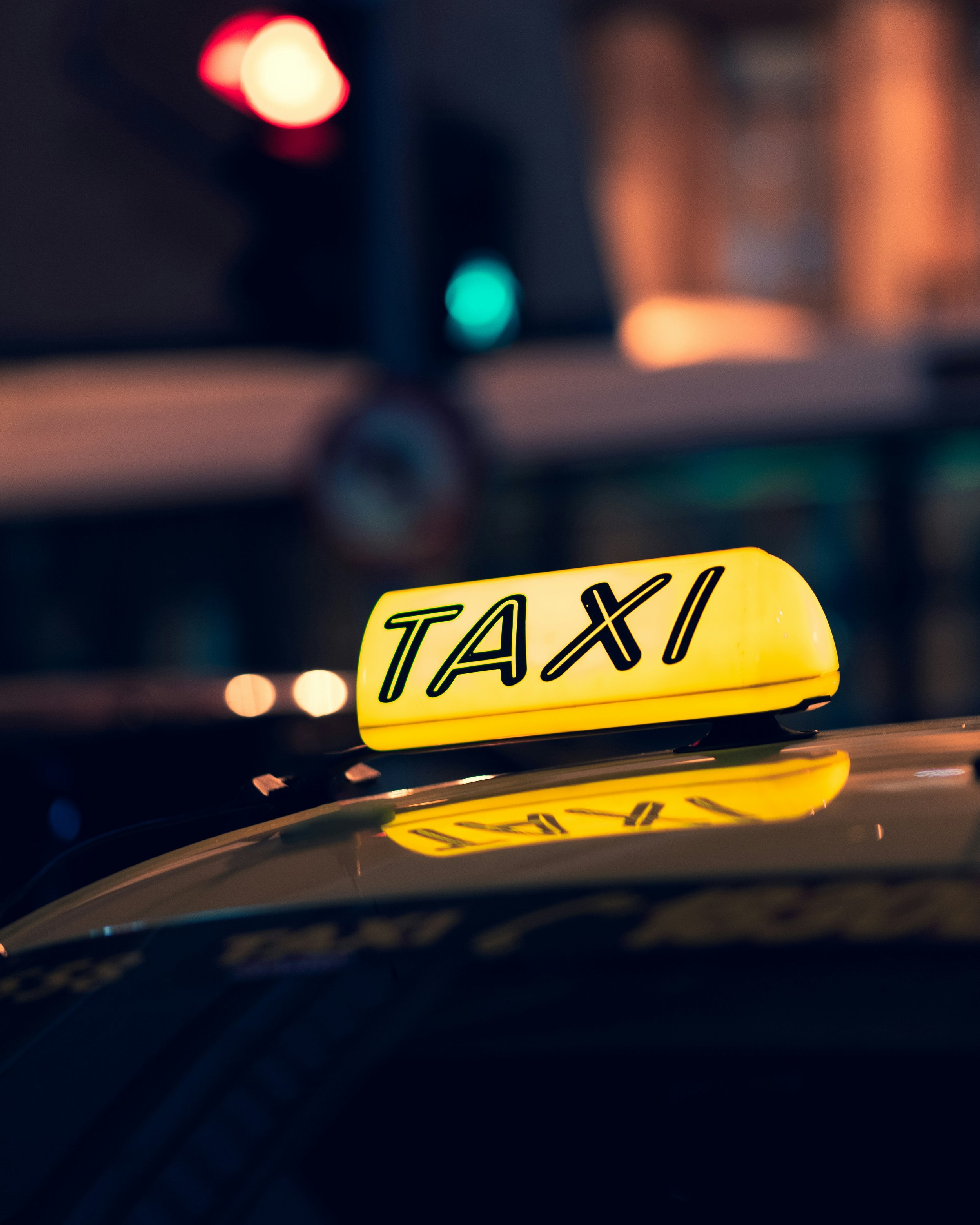 Taxi in Makry Gialos & Ierapetra - Yellow taxi sign reflecting on the car's dashboard at night with blurred colorful city lights in the background.