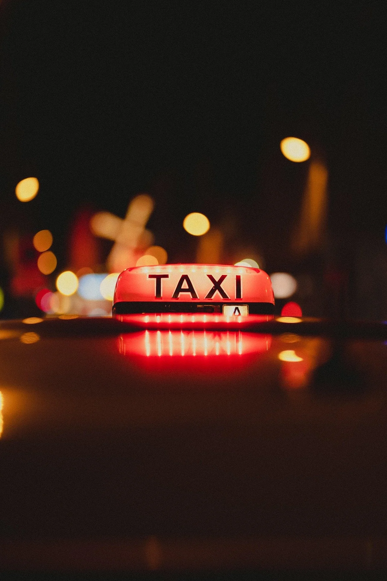 Taxi in Makry Gialos & Ierapetra - Close-up of a red taxi roof sign with the word 'TAXI' illuminated at night, blurred city lights in the background.