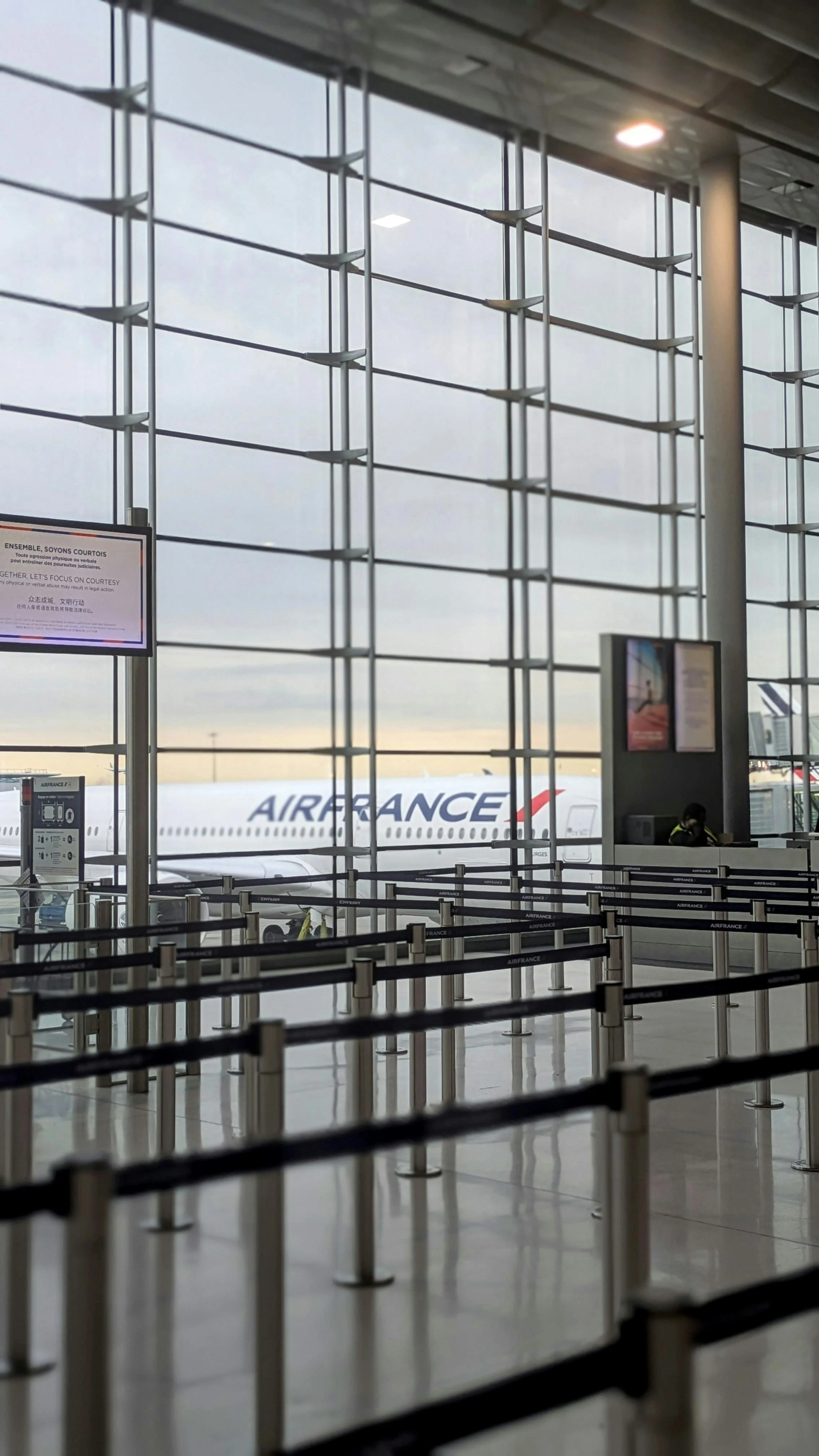 Taxi in Makry Gialos & Ierapetra - Interior of an airport terminal with empty queue barriers, a large window showing an airplane outside with the airline name 'AIRFRANCE' on its tail, and departure information screens.
