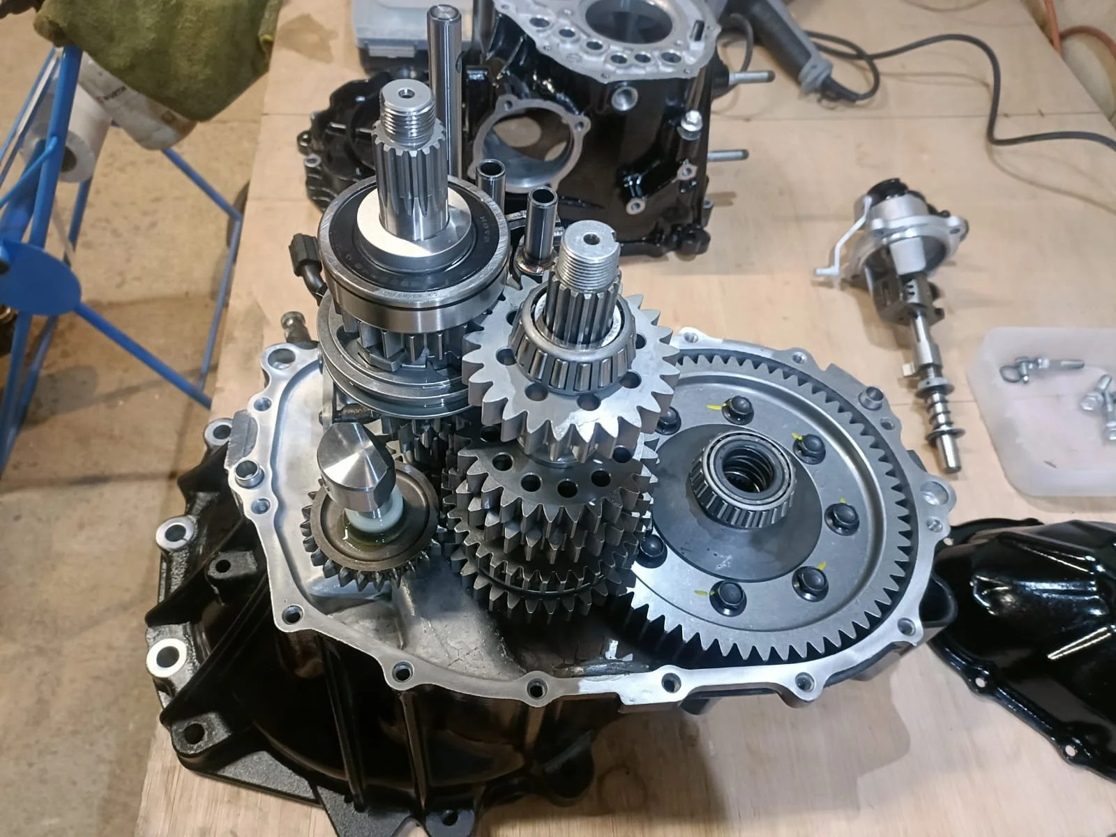 Disassembled motorcycle transmission with gears and shafts on a workbench.