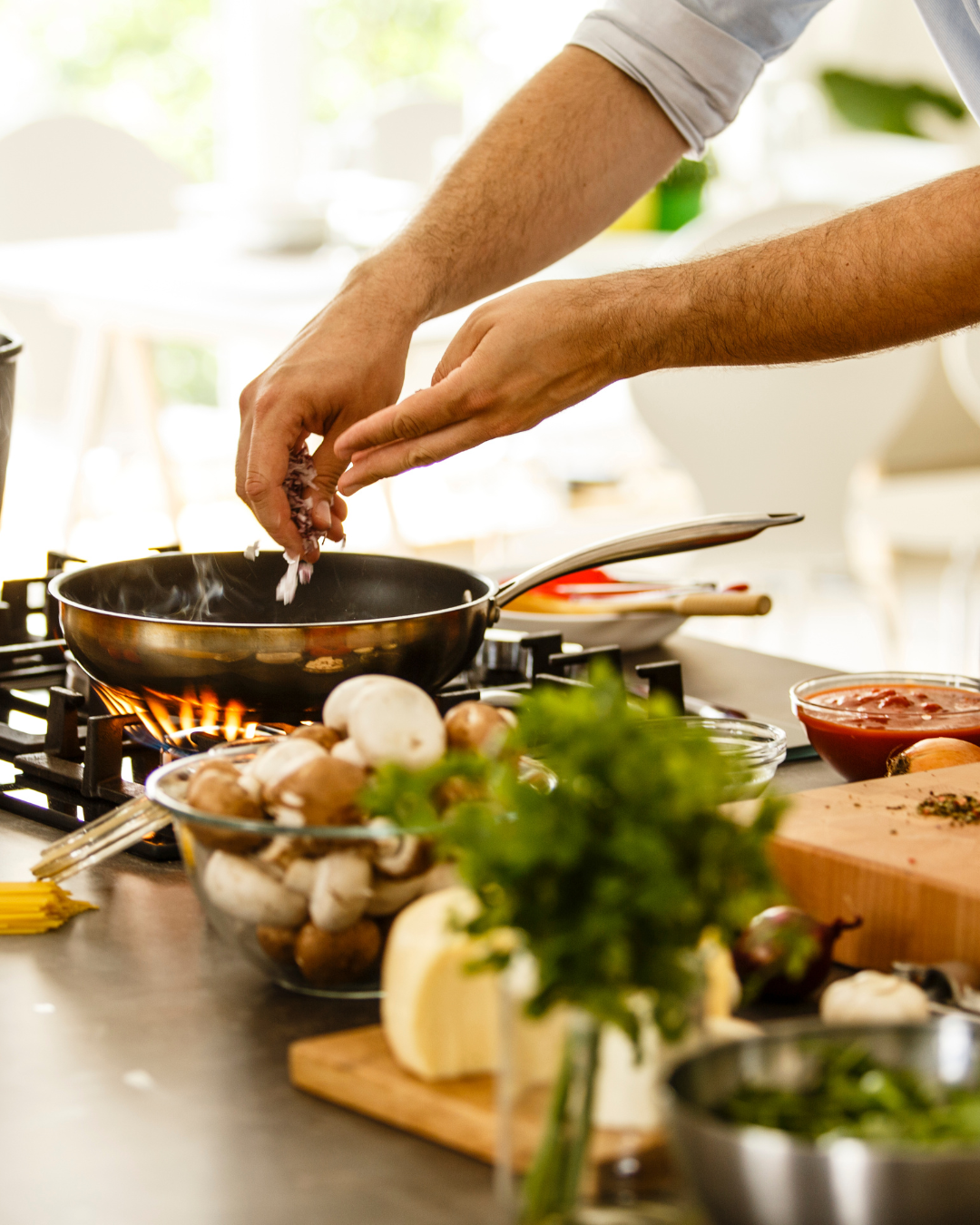 Person cooking on stove with vegetables, mushrooms, and pasta on countertop.