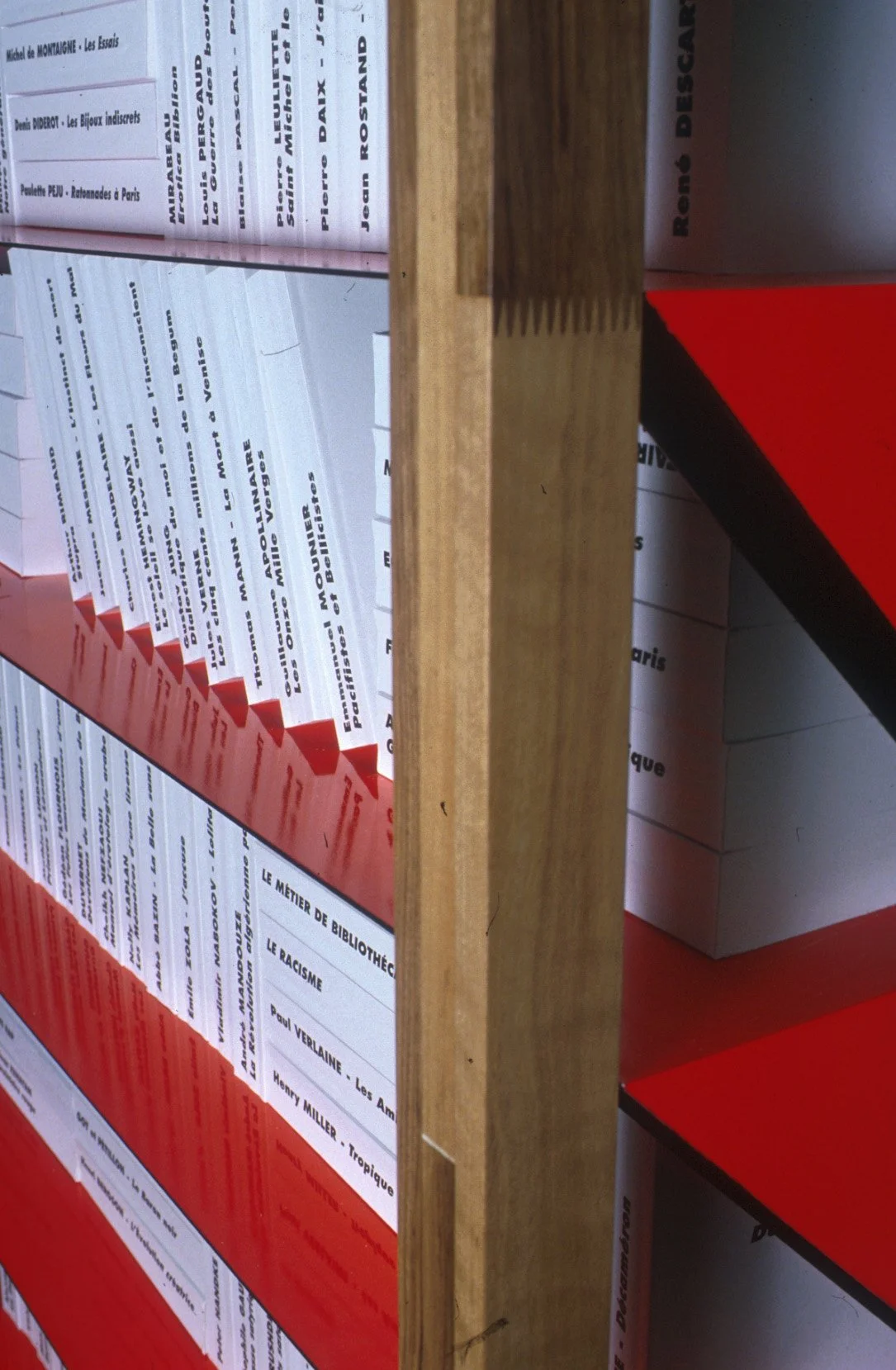 Une étagère en bois contenant plusieurs livres, dont certains sont rouges avec des titres en français. Le livre visible sur le côté droit a la mention 'Banque Descartes'.