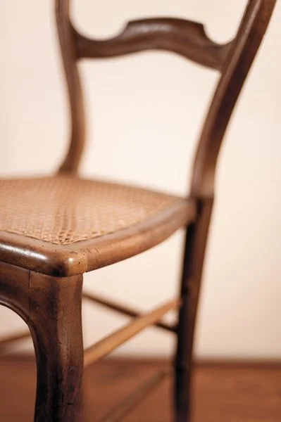 Chaise en bois avec assise en cannage devant un mur beige.