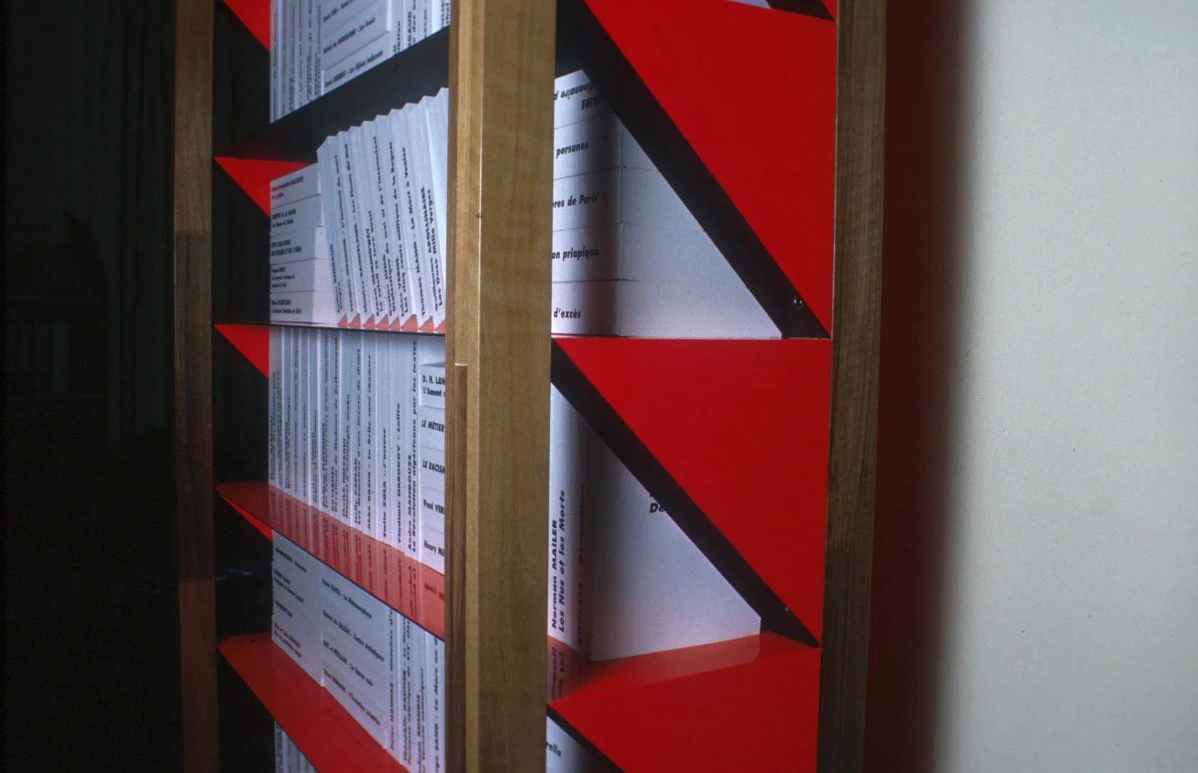 Une étagère en bois contenant plusieurs cartons de livre empilés verticalement, avec des titres visibles sur certains de ces cartons.
