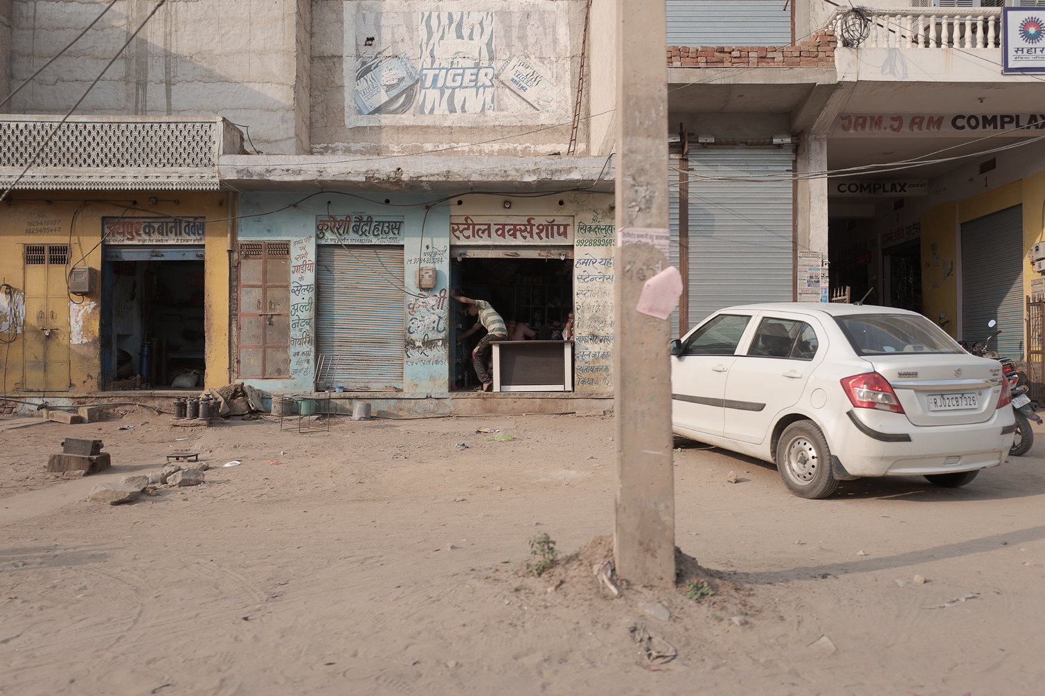 Une rue en Inde avec des boutiques fermées, une voiture blanche et un scooter, et des façades de bâtiments en mauvais état.