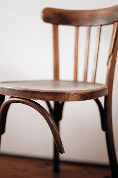 Chaise en bois avec dossier et assise en bois, placé contre un mur blanc.