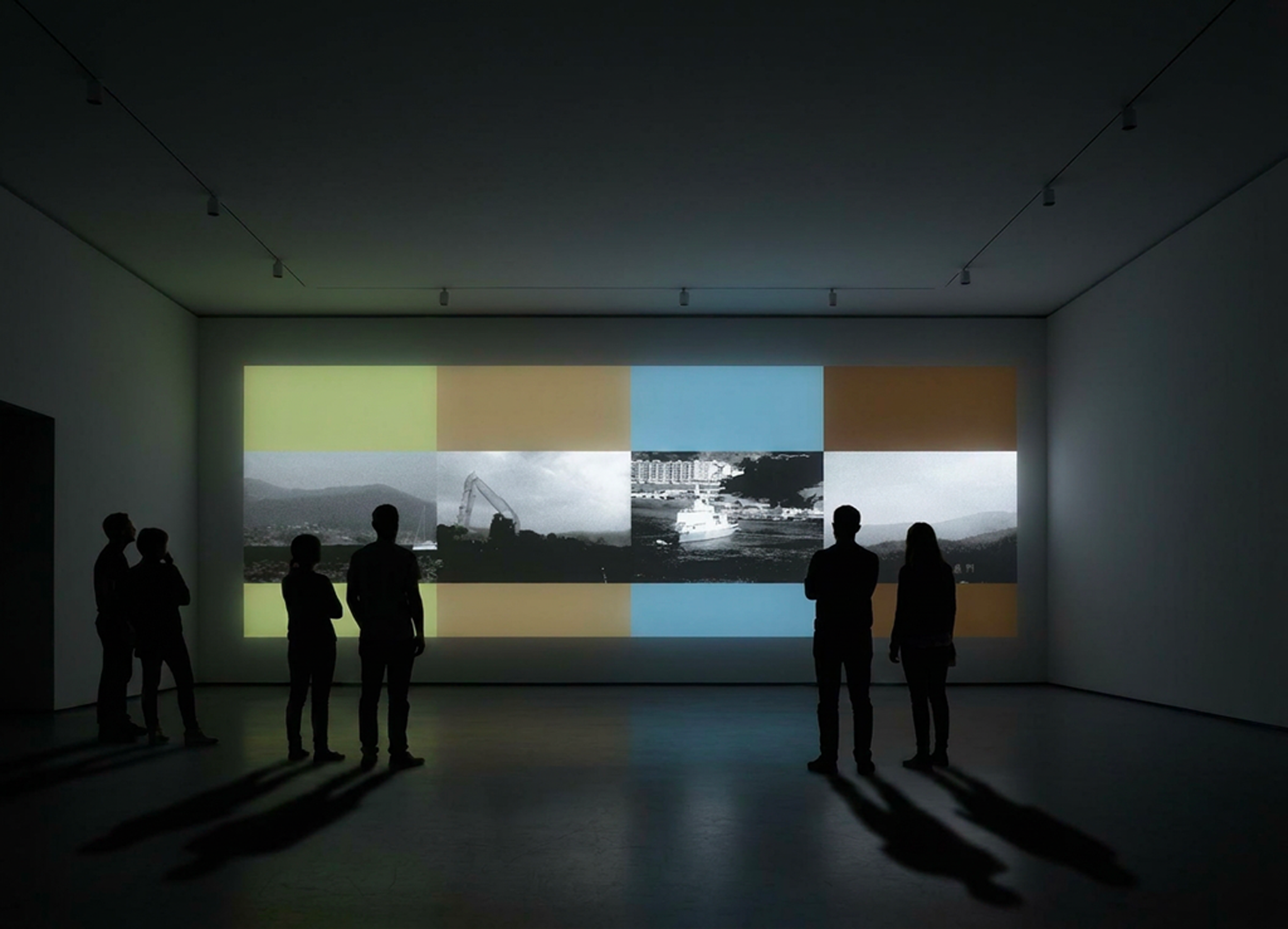 Groupe de personnes regardant une présentation ou une vidéo sur un mur d'écran dans une pièce sombre.