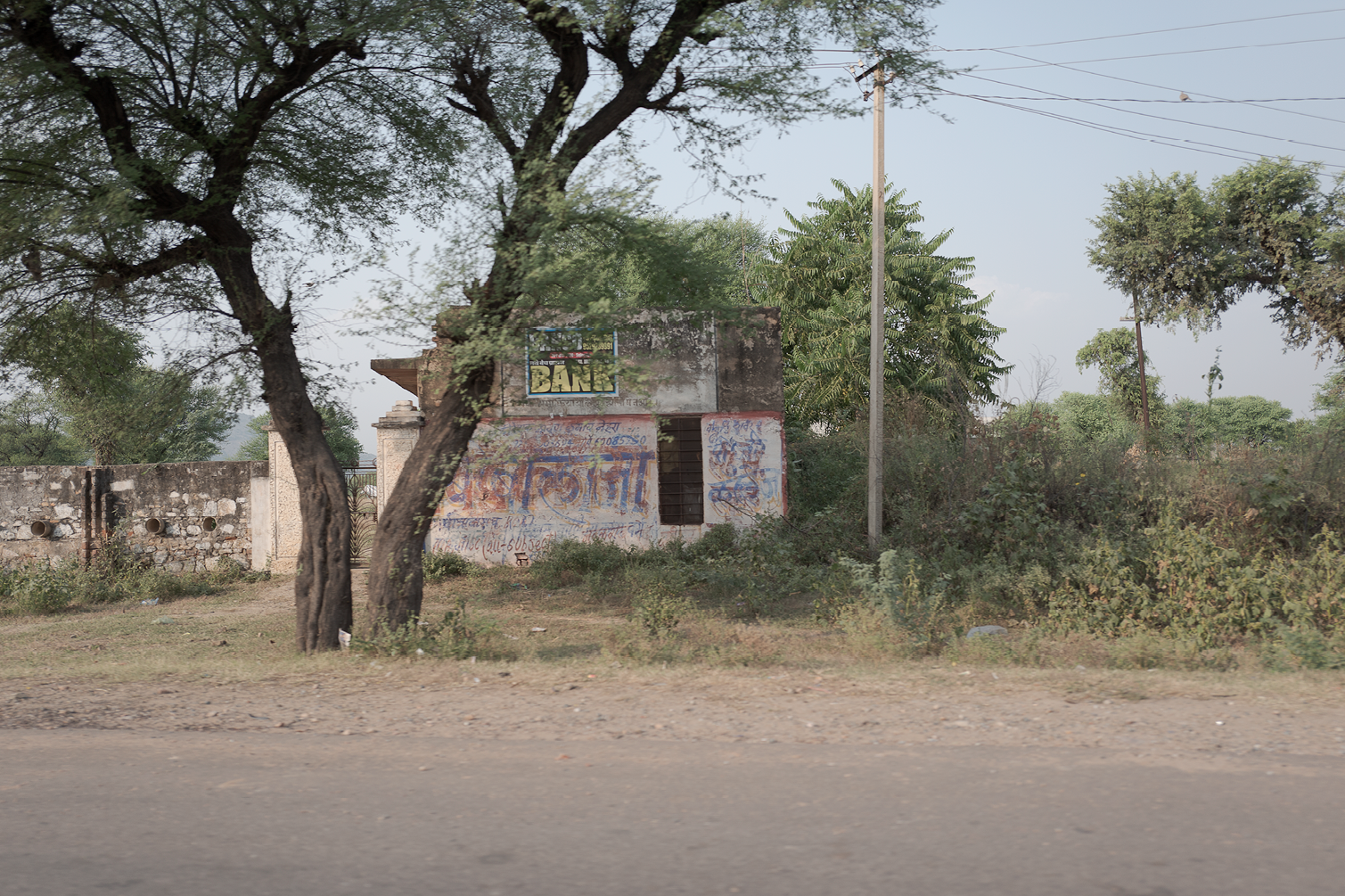 Une petite maison en pierre, entourée de végétation, avec un mur en pierre et des graffitis, avec des arbres et des poteaux électriques