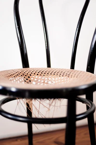Chaise en bois avec assise tissée, contre un mur blanc.