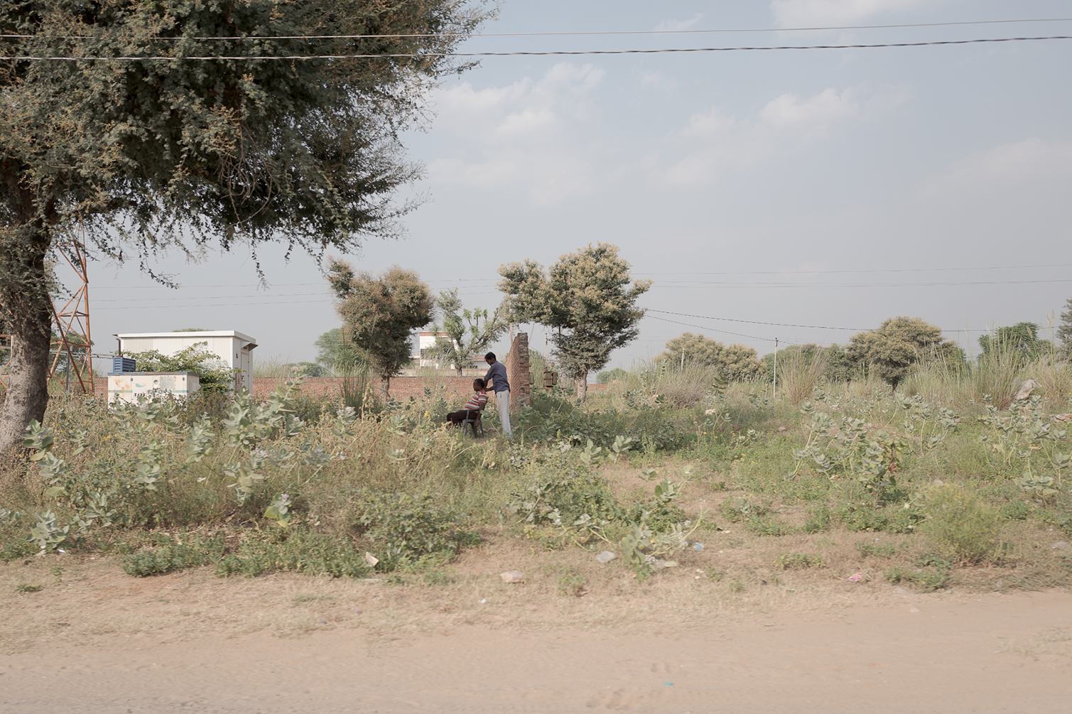 Deux enfants jouent dans un champ avec des arbres et un ciel partiellement nuageux.