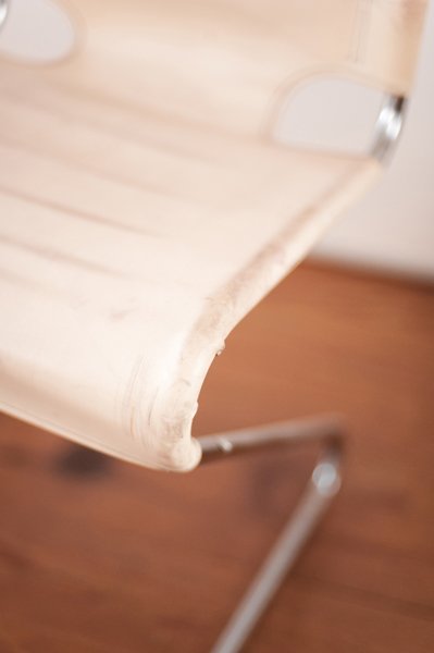 Détail d'une chaise en bois clair avec une partie cassée ou endommagée au coin.