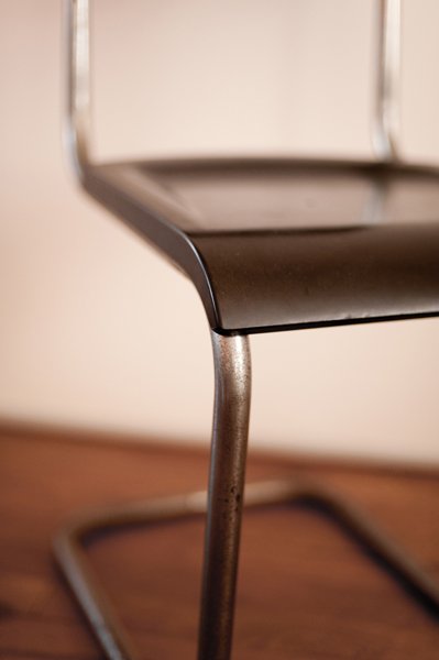 Premier plan d'une chaise de bureau en métal et plastique, vue de côté, avec un sol en bois en fond.