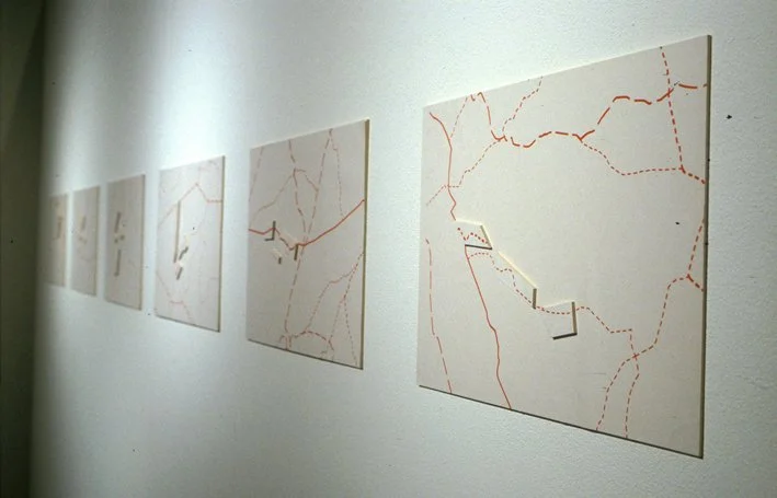 Une série d'œuvres d'art abstraites exposées sur un mur blanc, représentant des lignes rouges sur des fonds clairs.