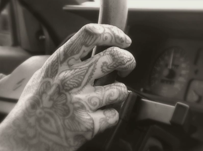 Une main tatouée tenant le volant d'une voiture.