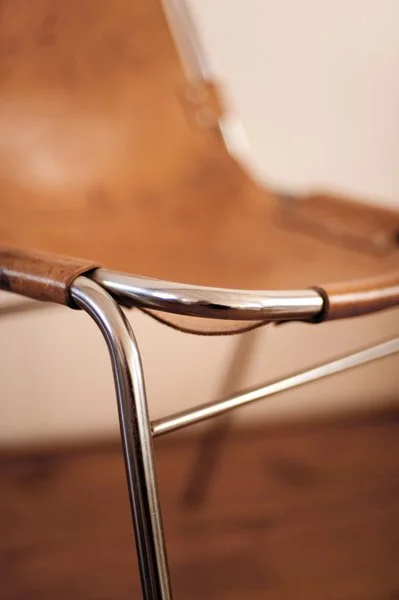 Close-up d'une chaise en cuir et métal avec un siège en cuir brun et un cadre en métal chromé.
