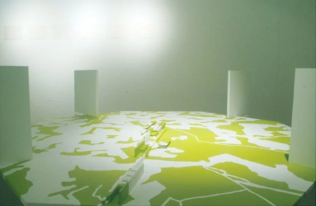 Modèle de carte géographique ou plan urbain en 3D, avec des murs blancs et une surface représentant un paysage ou une ville en vert et blanc.