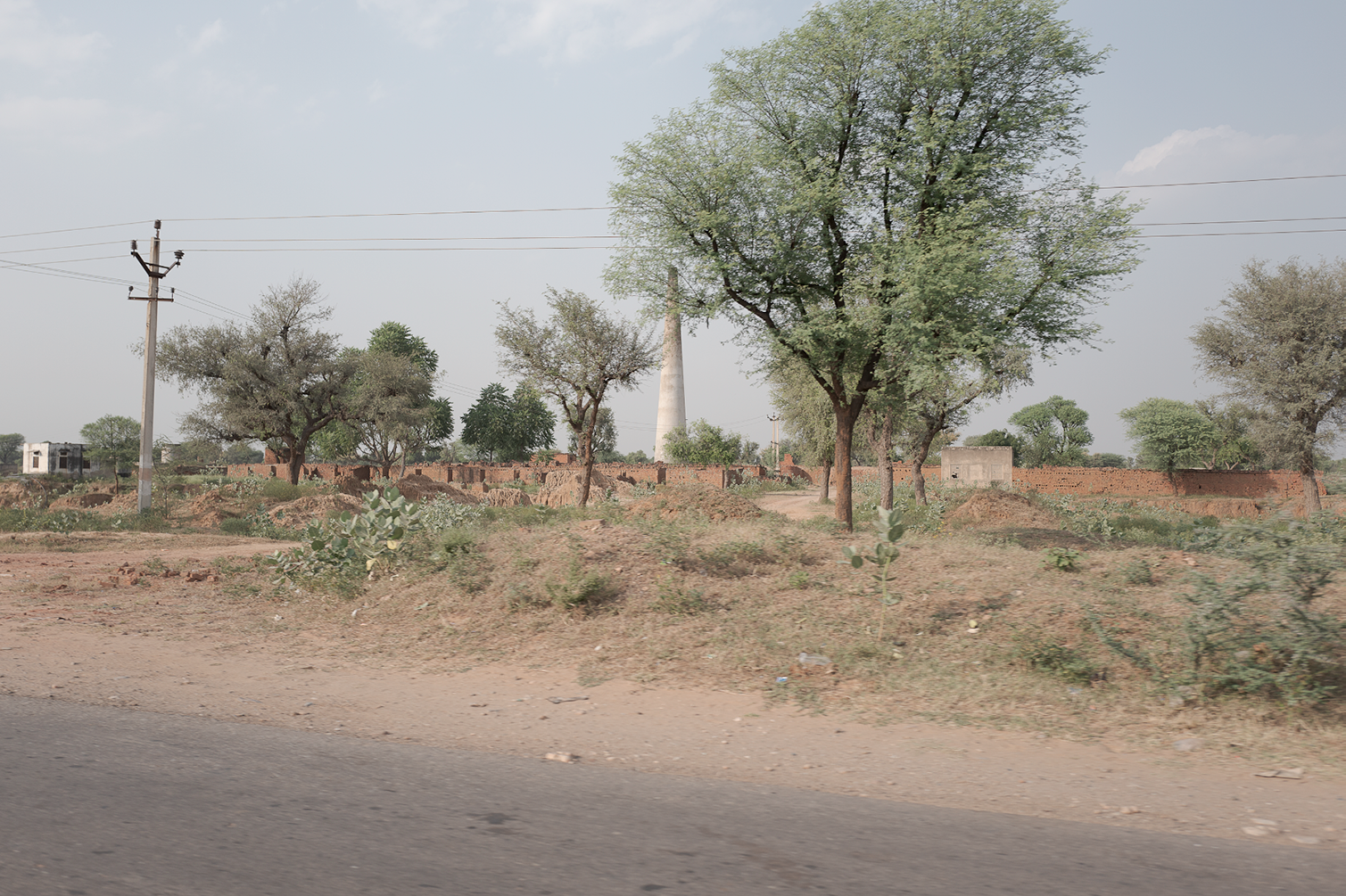 Paysage rural avec des arbres, une route, et une cheminée de centrale électrique en arrière-plan, dans un environnement semi-aride.