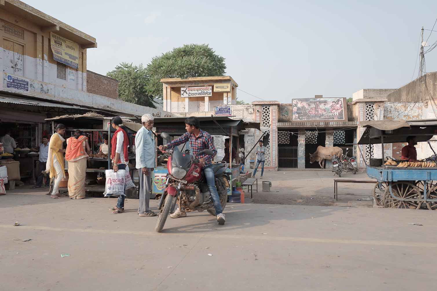 Scène de marché en Inde avec des vendeurs, des clients, une moto, une vache et des étals de nourriture