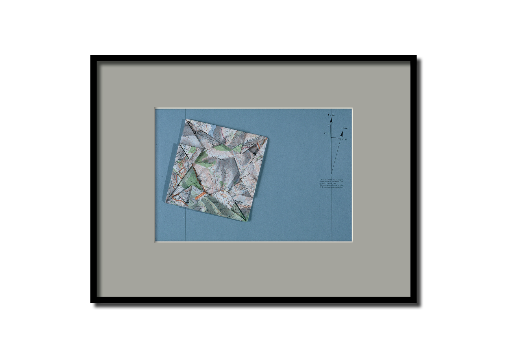 Une carte topographique pliée en forme d'origami posée sur une grande carte bleue