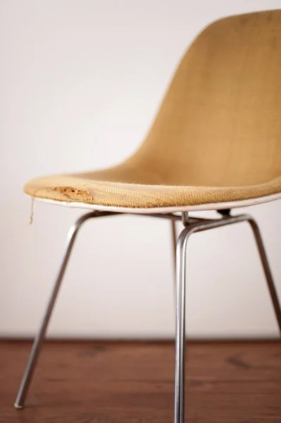 Chaise beige avec des jambes en métal, en mauvais état à cause de l'usure sur le bord du siège.