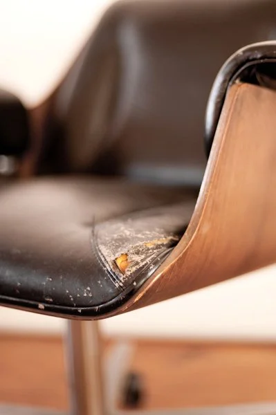 Chaise usée avec poussière et débris sur l'assise en faux cuir et bois.