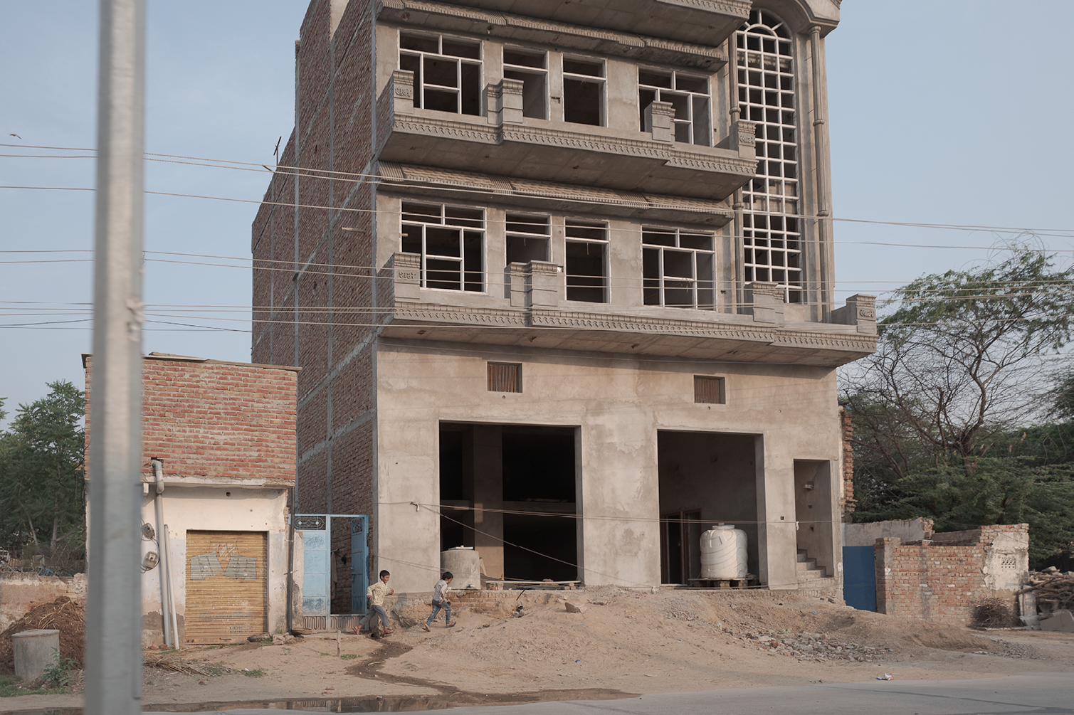 Bâtiment en construction avec plusieurs étages, encadrements de fenêtres en cours d'installation, construction en cours dans un environnement urbain, avec des enfants jouant à proximité.