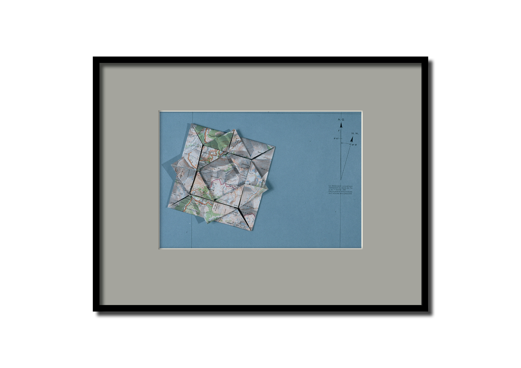 Une carte géographique pliée en origami posé sur une surface bleue.