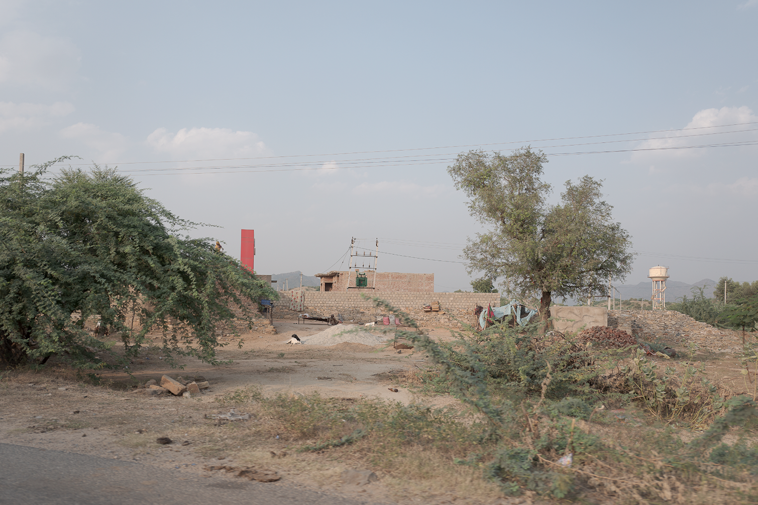 Paysage rural avec des arbres, une maison en construction, une tour d'eau, et un ciel clair.