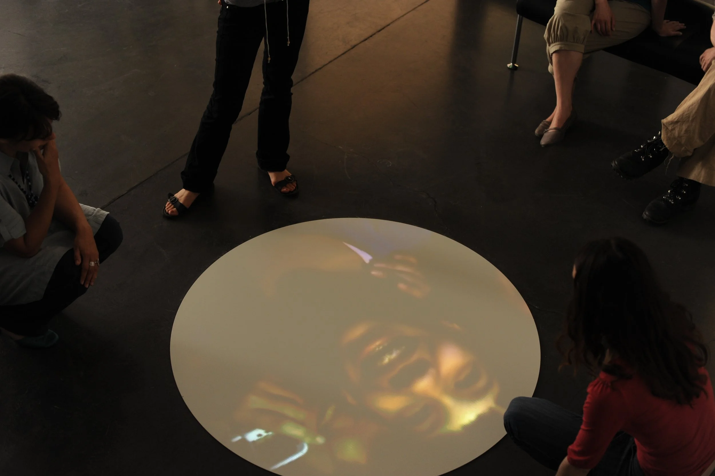 Groupe de personnes assises ou debout autour d'une surface rondes, probablement un écran ou une table, dans un environnement intérieur.