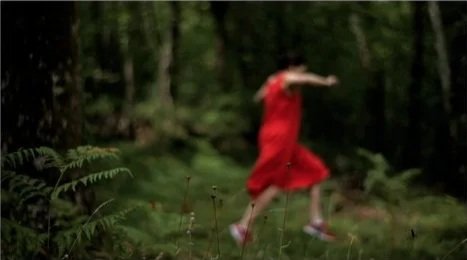 Une fille en robe rouge courant ou sautant dans une forêt